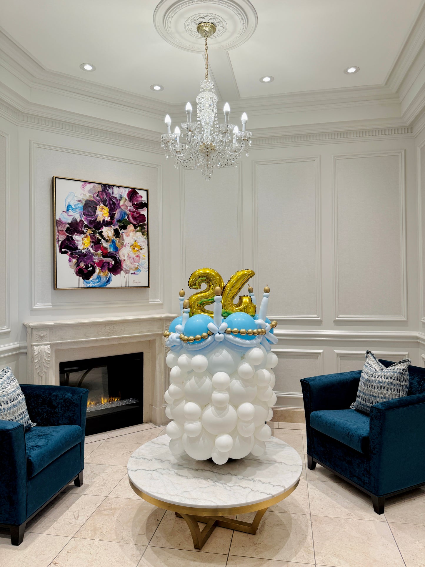 Decorative cake with balloons and number '24' in a stylish room with a chandelier and artwork.
