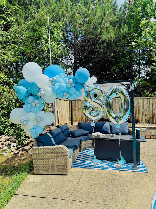 Outdoor setting with blue and white balloons and a '80' balloon in a garden.