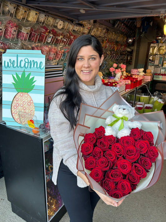 Heart-shaped bouquet of fresh red roses wrapped in floral paper with a teddy bear included.