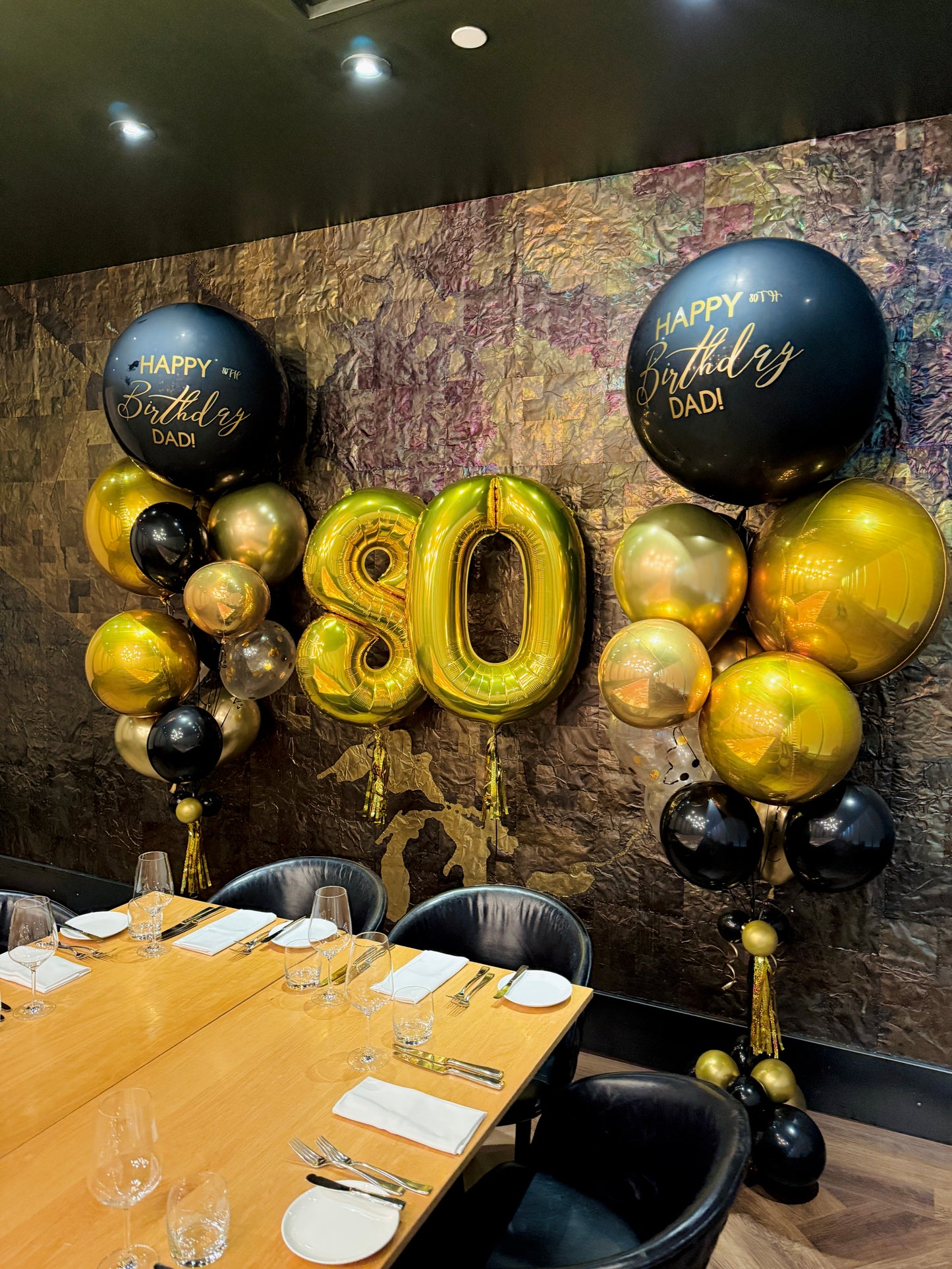 Decorative balloons with 'Happy Birthday DADI' and number '80' in a dining setting.