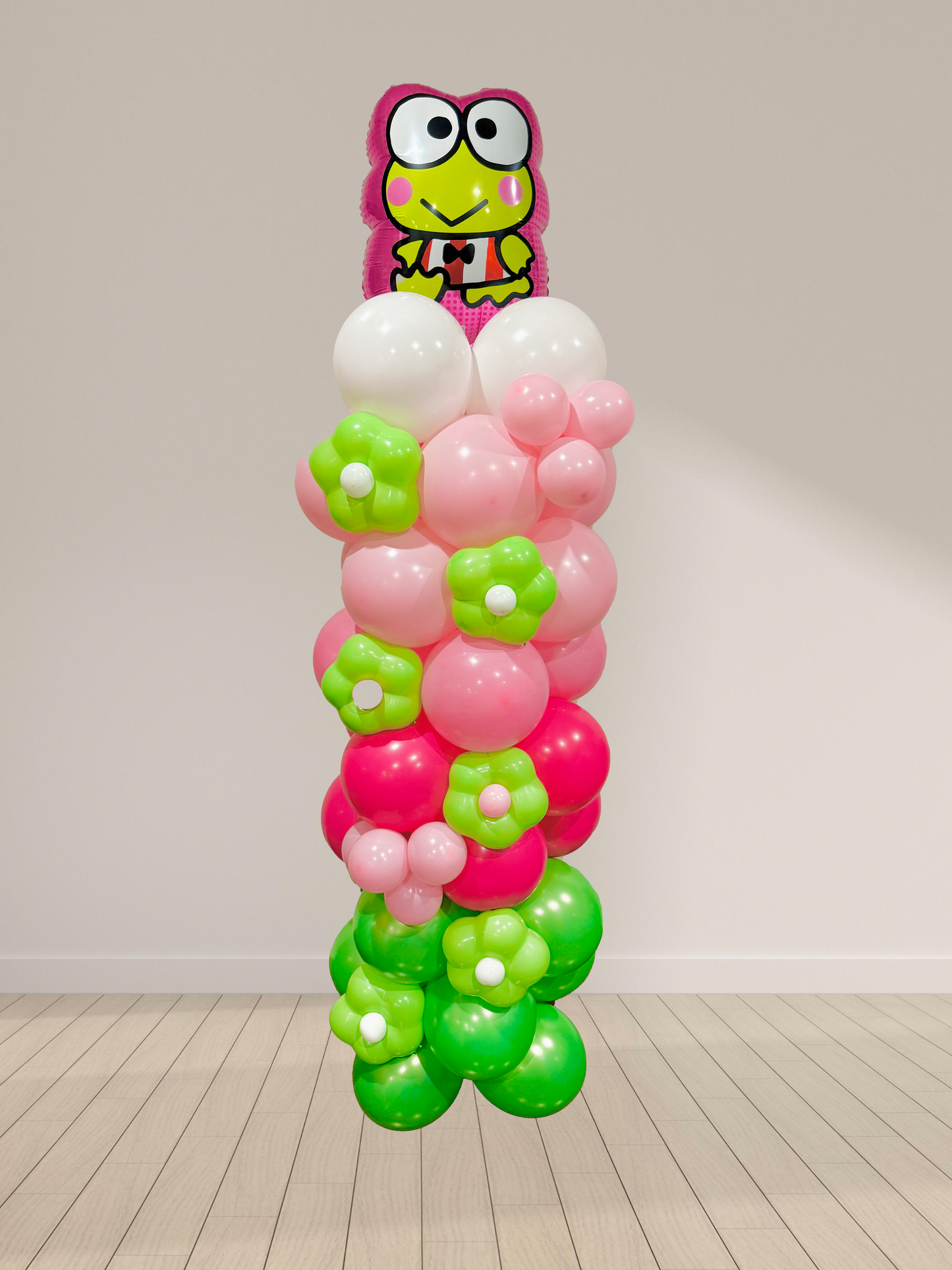 Balloon column with pink and green flowers and a cartoon frog character on top against a white wall.