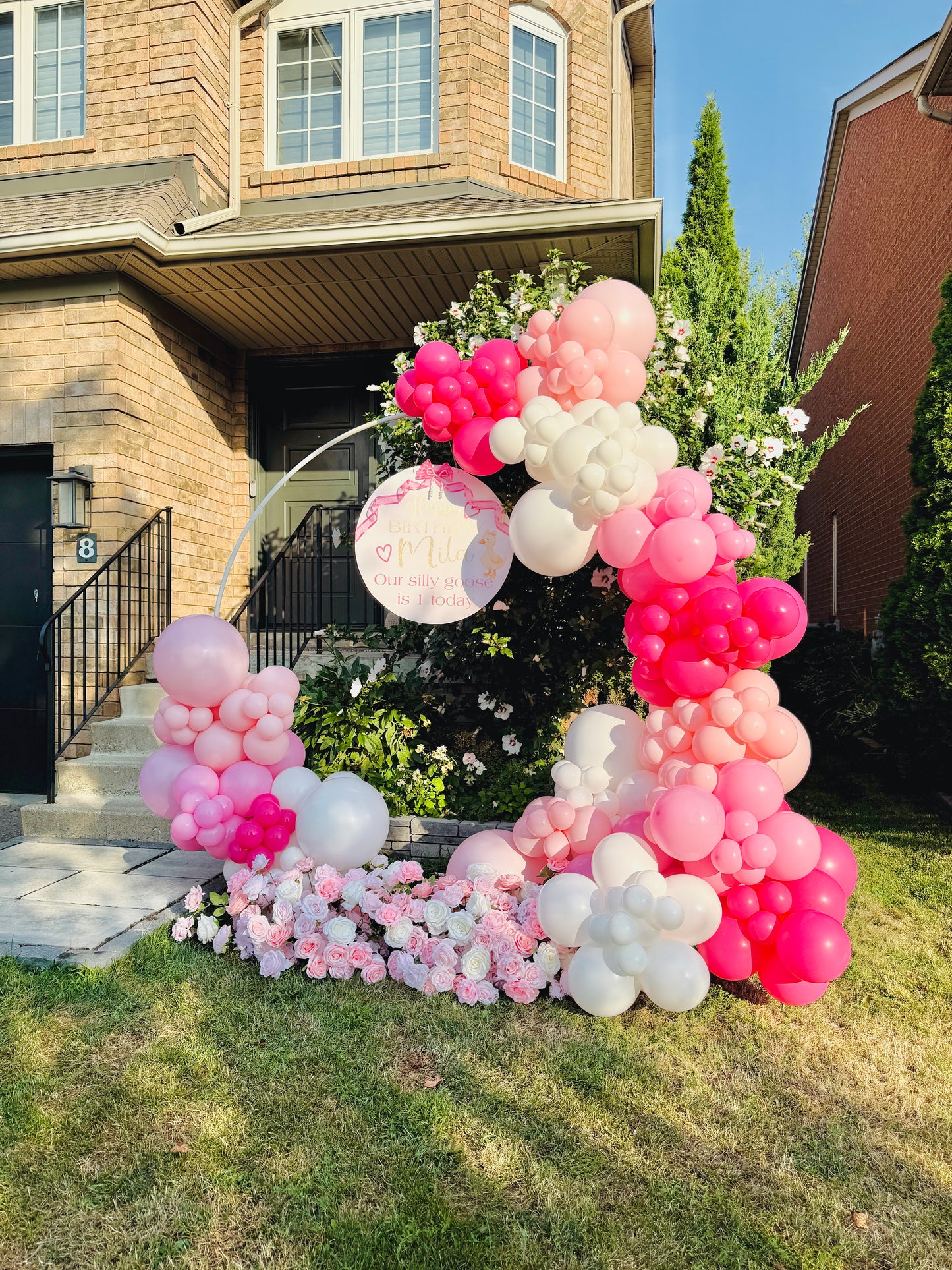 Balloon arch with pink, white, and red balloons in front of a house.