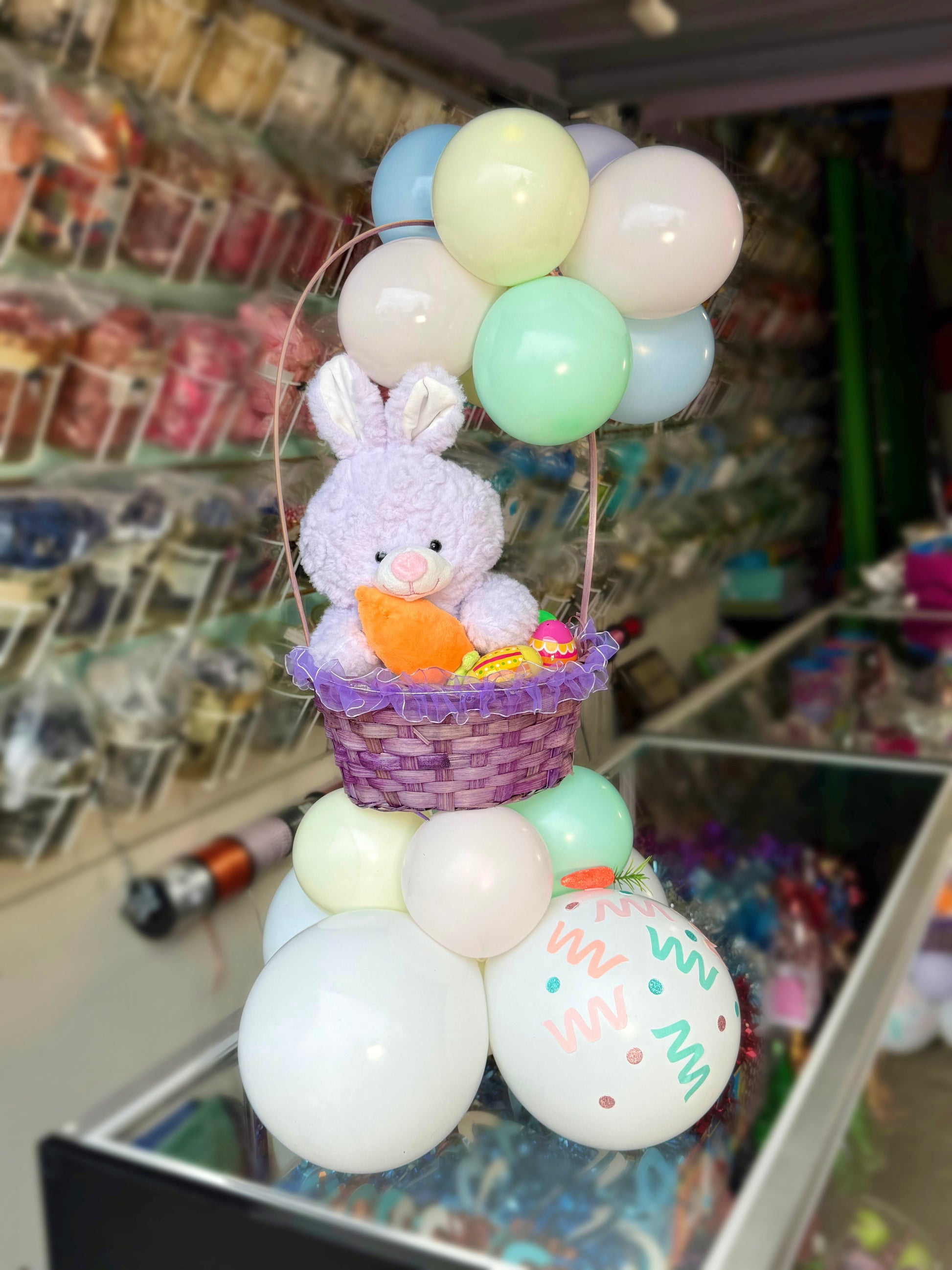 Decorative display with pastel balloons, a plush bunny, and a carrot in a store setting.