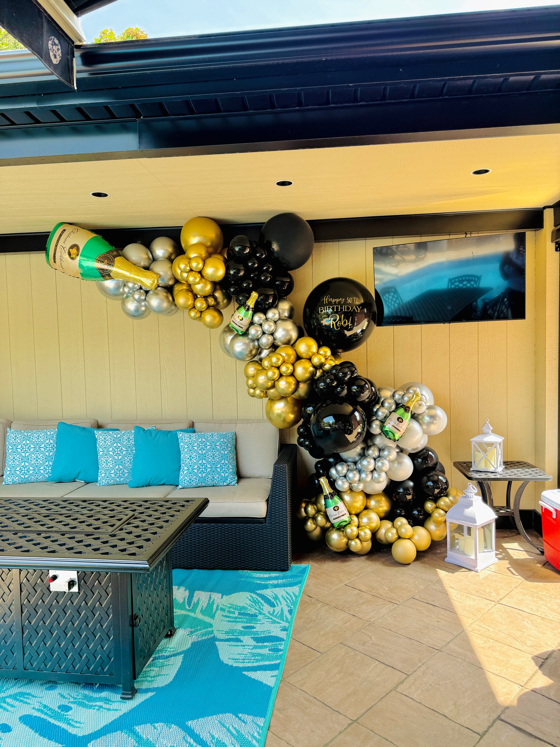 Decorative balloon arch with gold, black, and silver balloons in a patio area.