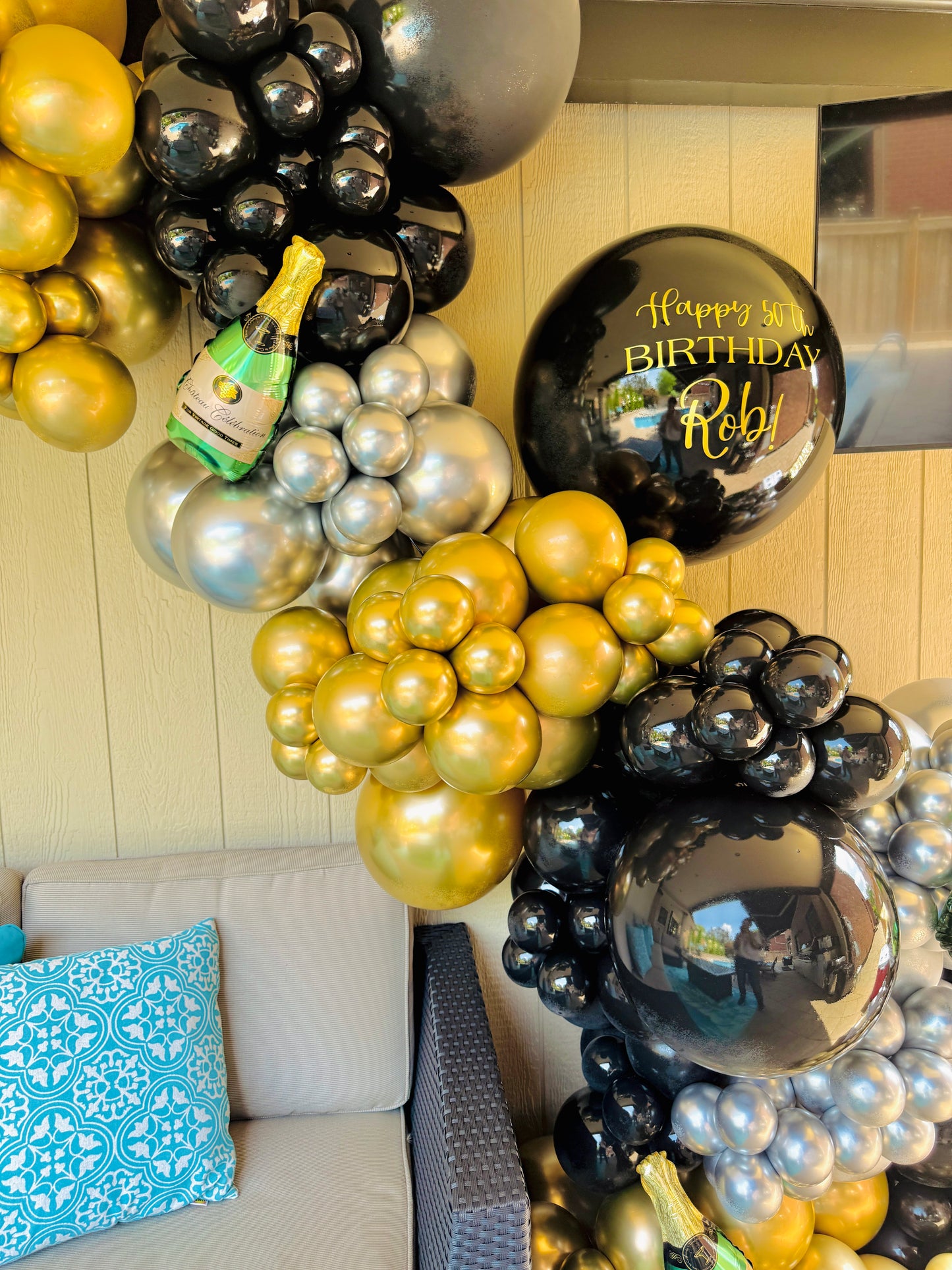 Balloon arch with gold, silver, and black balloons in a living room setting.
