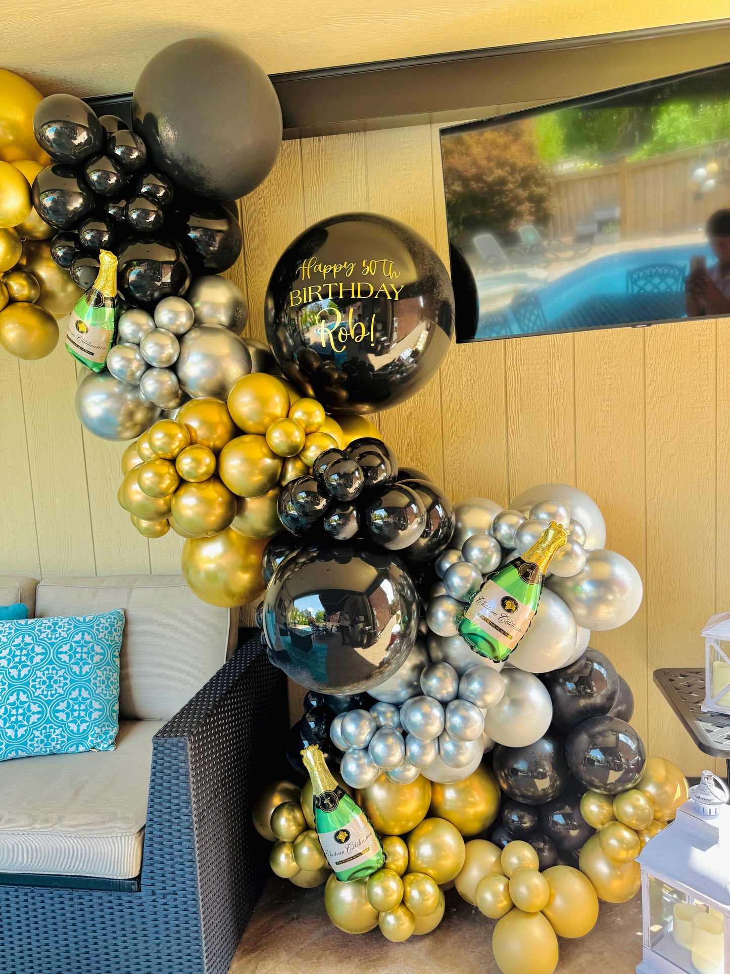 Balloon arrangement with champagne bottles and 'Happy 61st Birthday' balloon in a room.