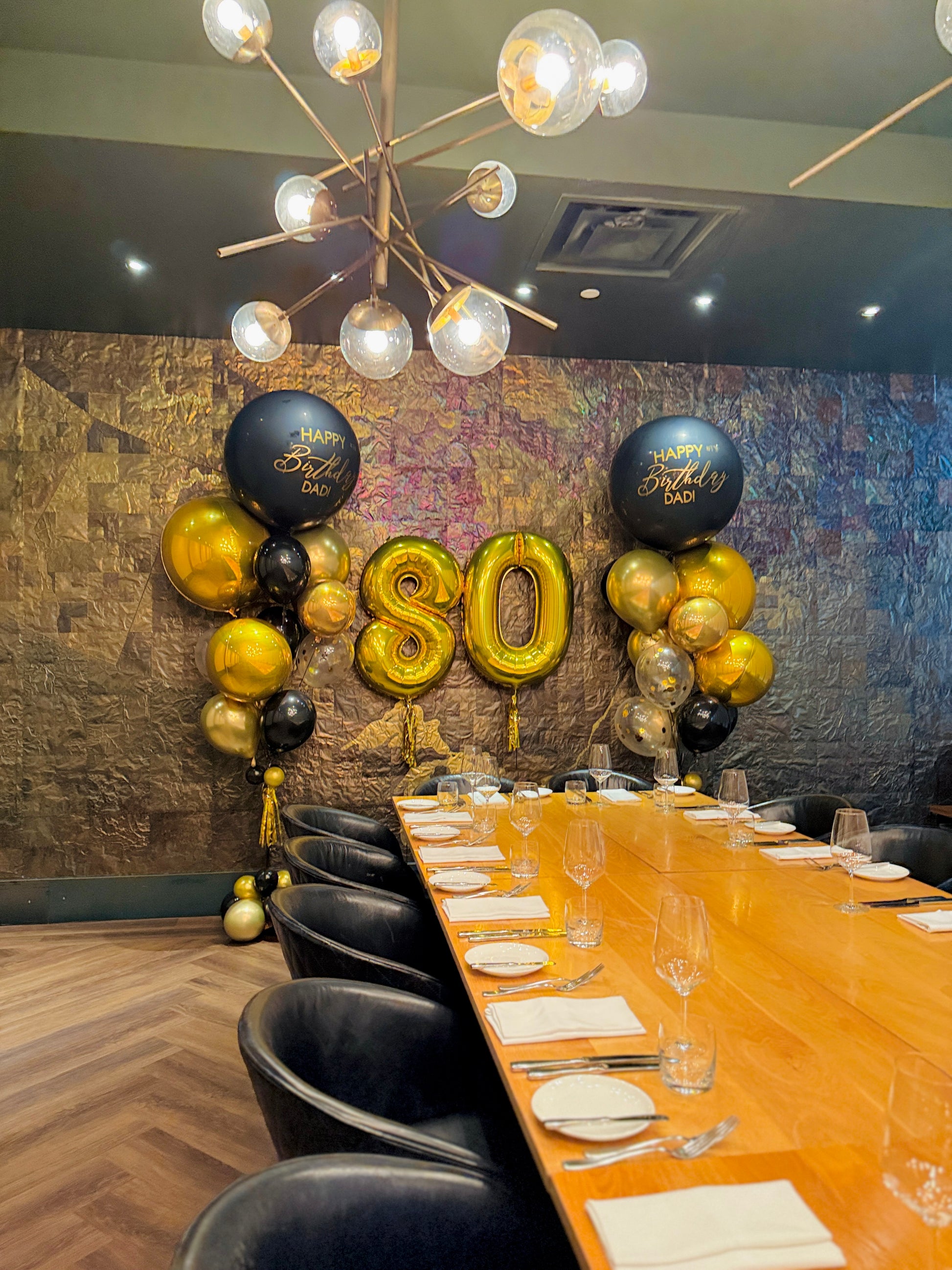 Dining room with a table set for a celebration, featuring gold and black balloons with 'Happy Birthday' and number '80'.