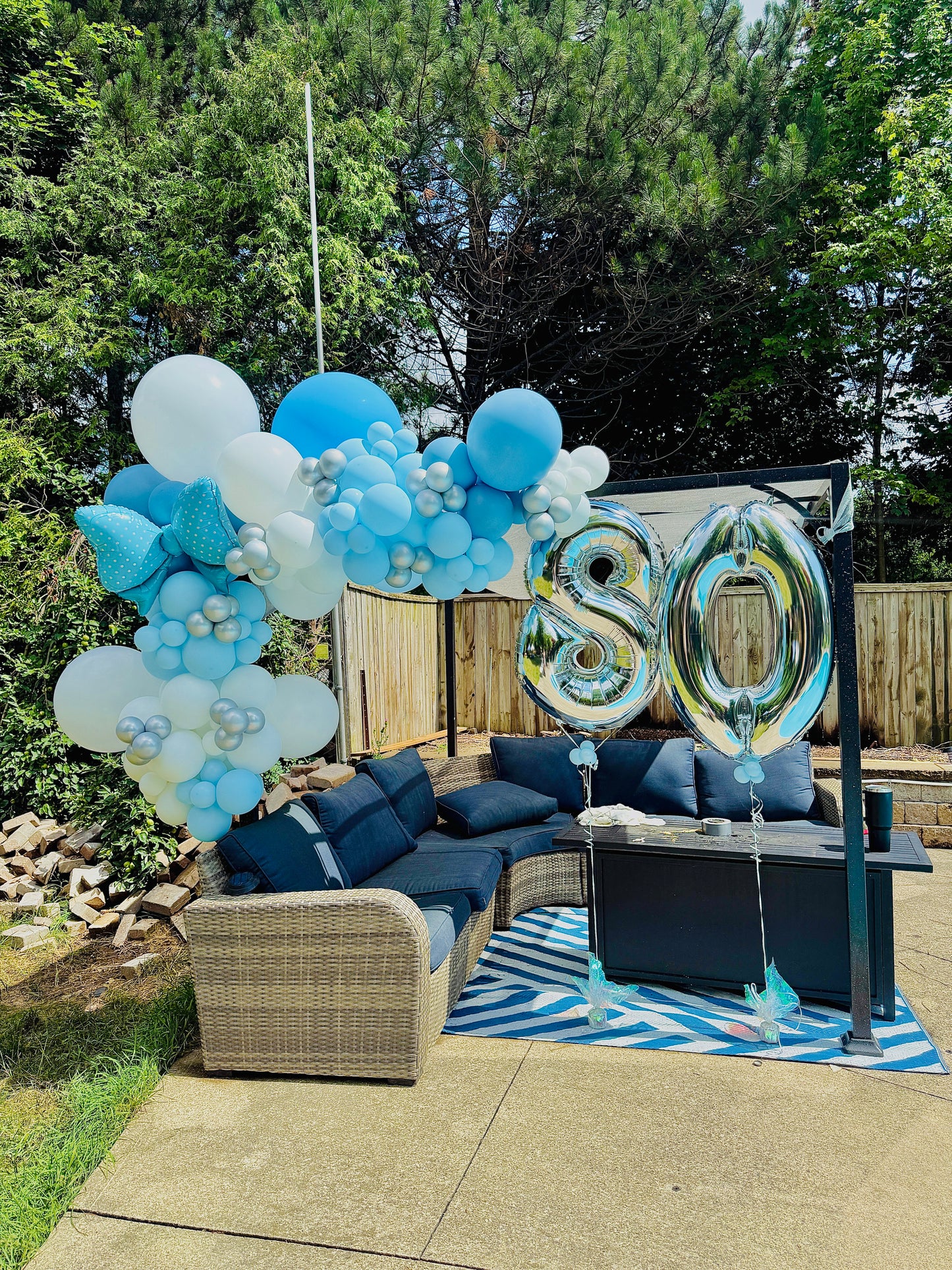 Outdoor setting with blue and white balloons and '80' balloons on a patio.