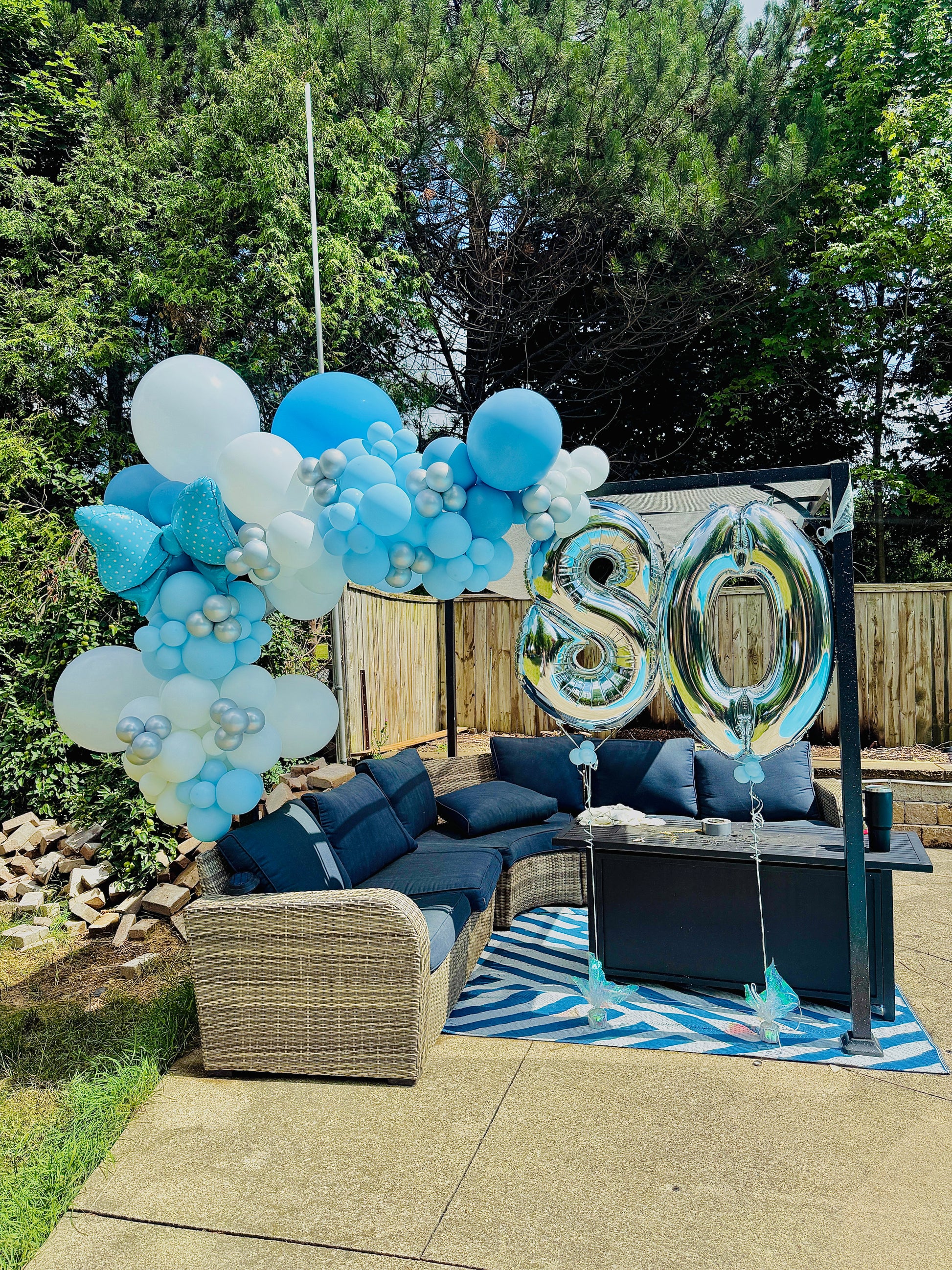 Outdoor setting with blue and white balloons and '80' balloons on a patio.
