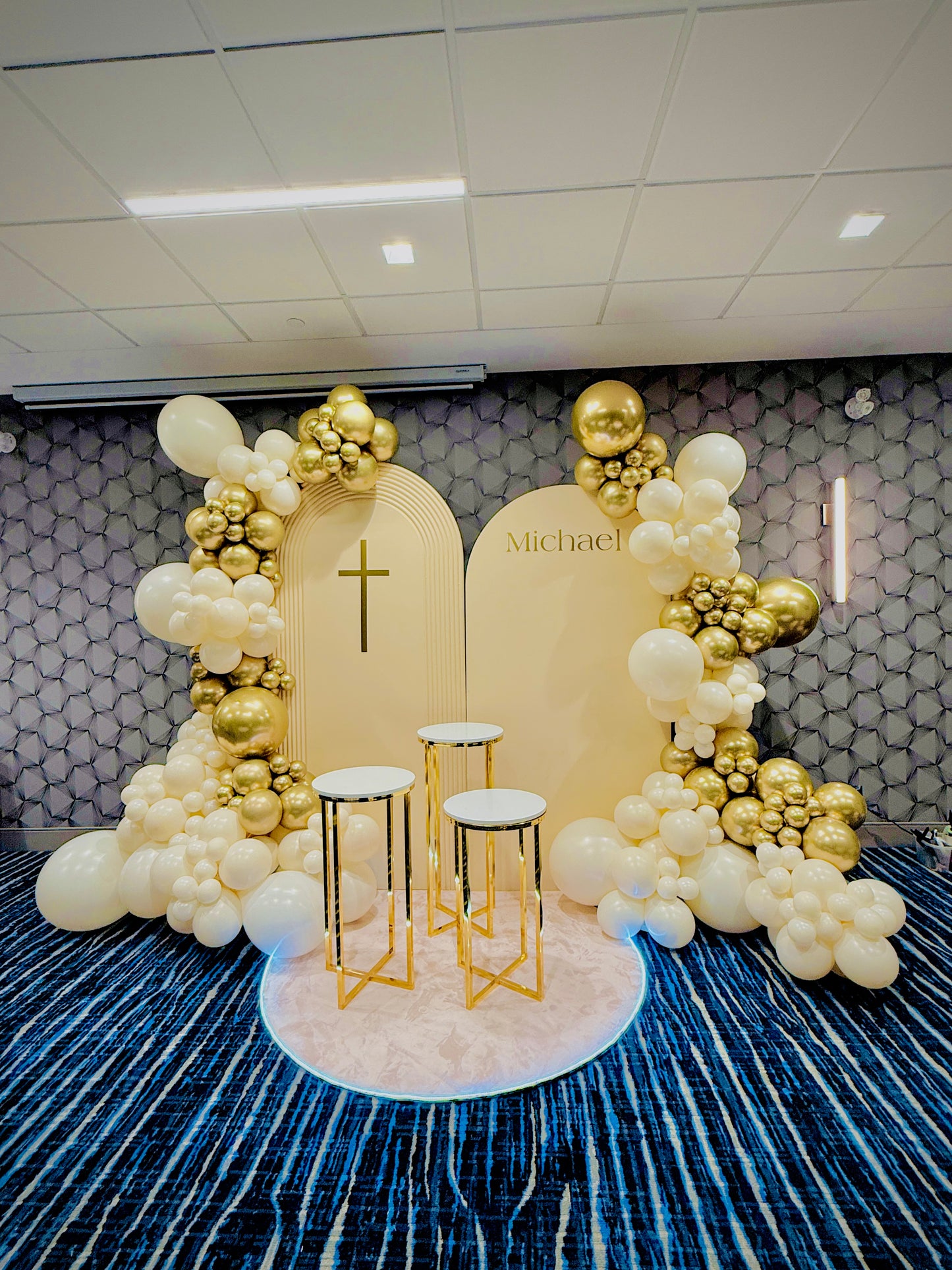 Decorative arch with balloons and a cross on a patterned wall.