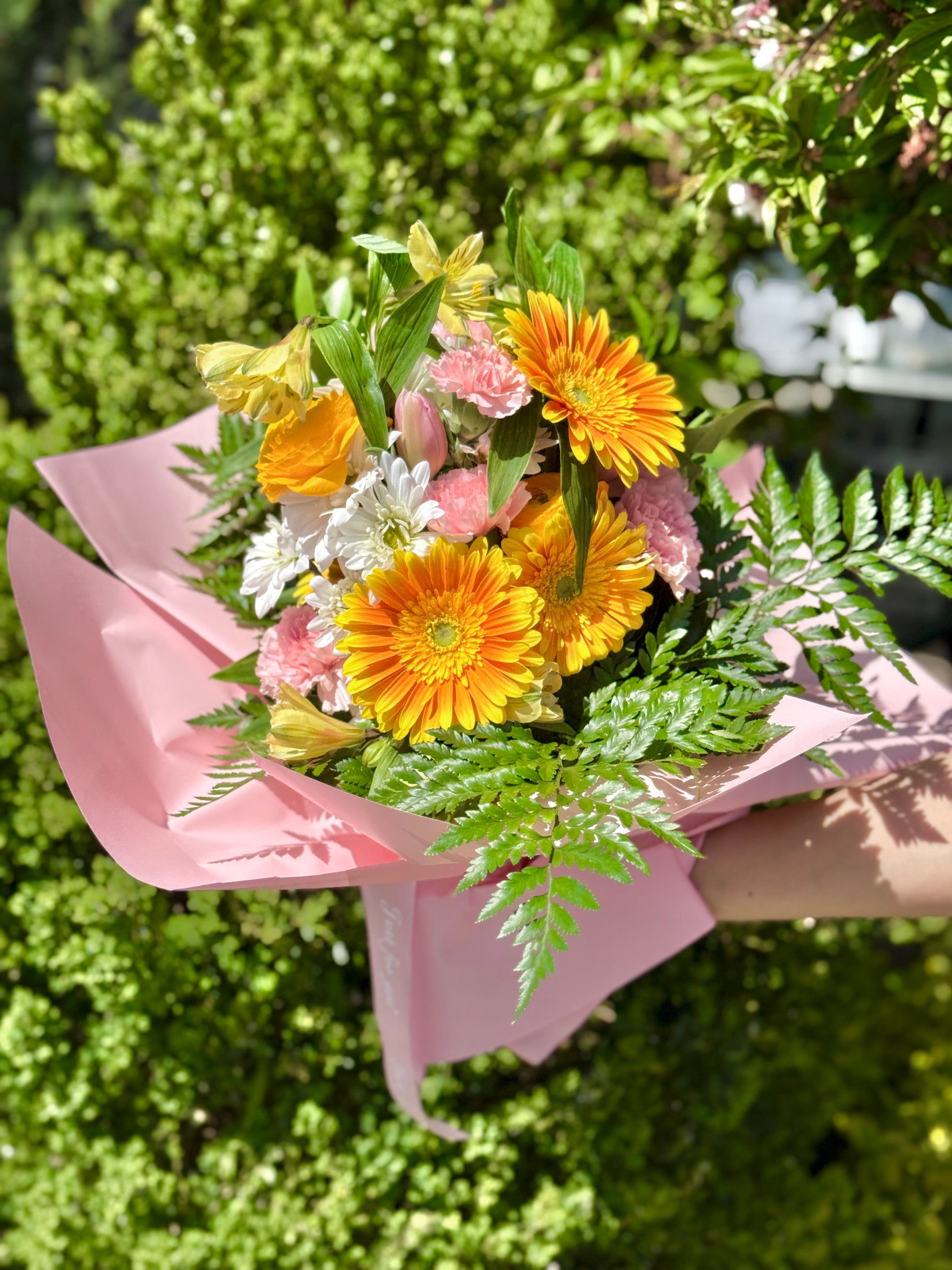 Bouquet of flowers with yellow gerberas and greenery wrapped in pink paper.
