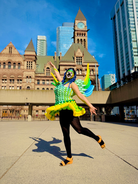 Person in a colorful costume dancing in an urban setting with tall buildings in the background