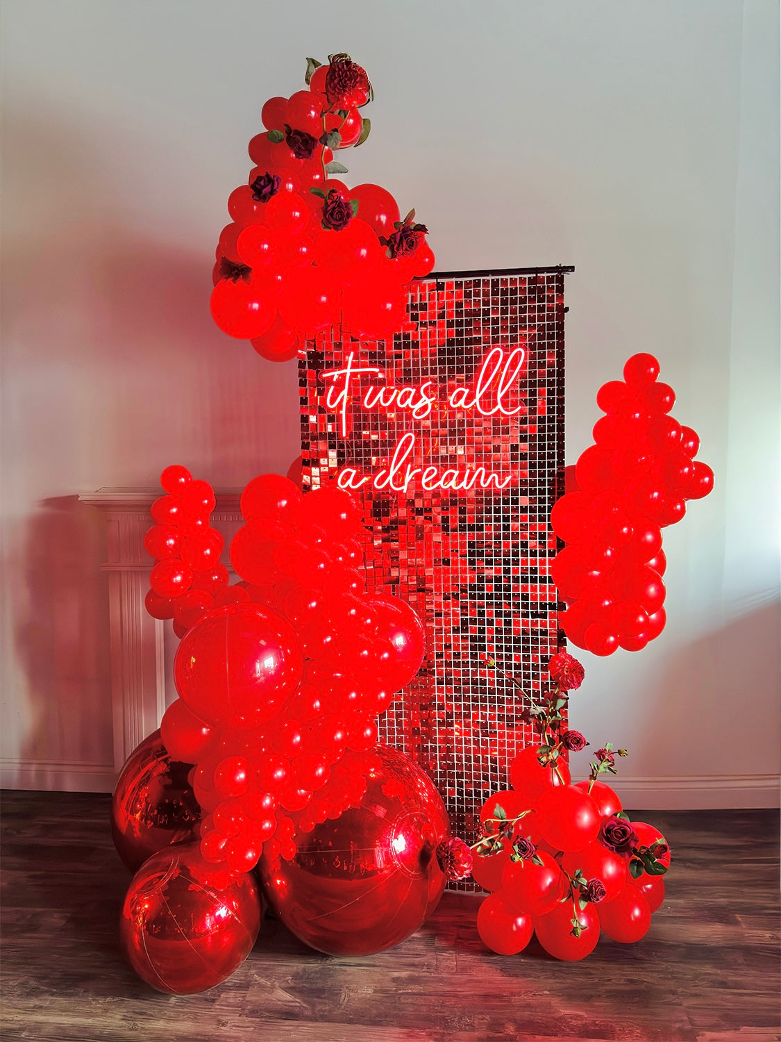 Luxury Red Shimmery Wall Balloon Installation with a red sequin wall, premium balloon garland, LED neon sign, florals, and mirror balls for an elegant event setup.