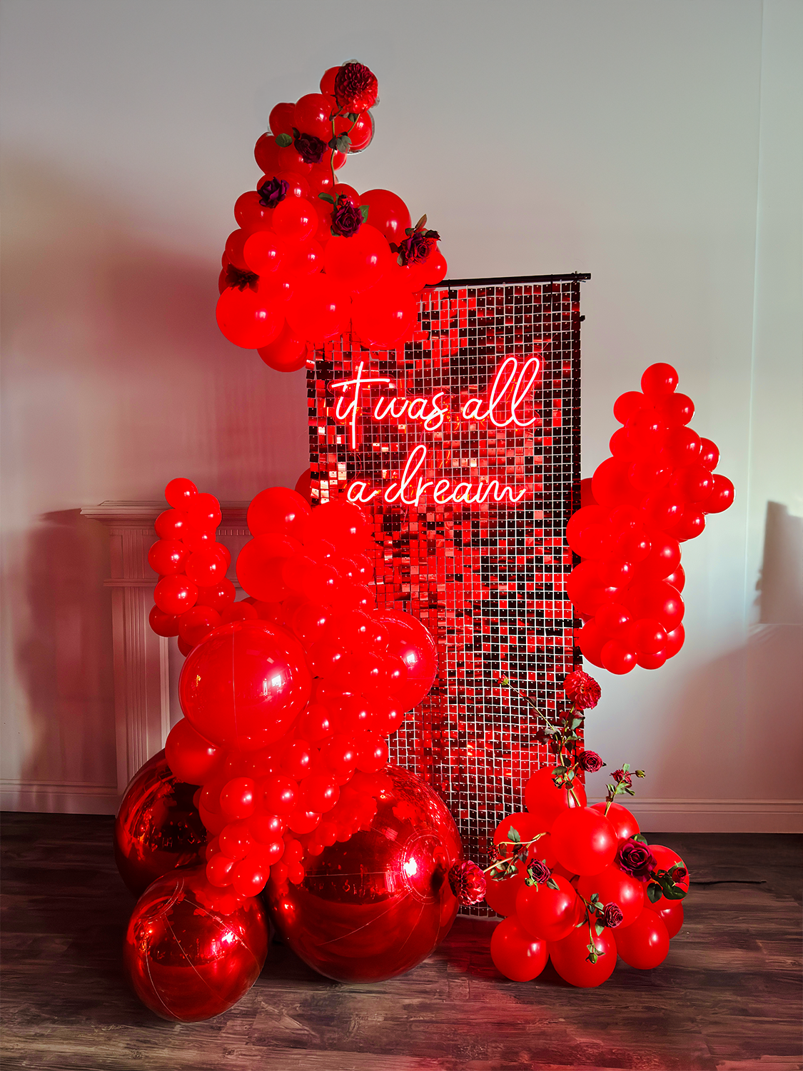 Luxury Red Shimmery Wall Balloon Installation with a red sequin wall, premium balloon garland, LED neon sign, florals, and mirror balls for an elegant event setup.