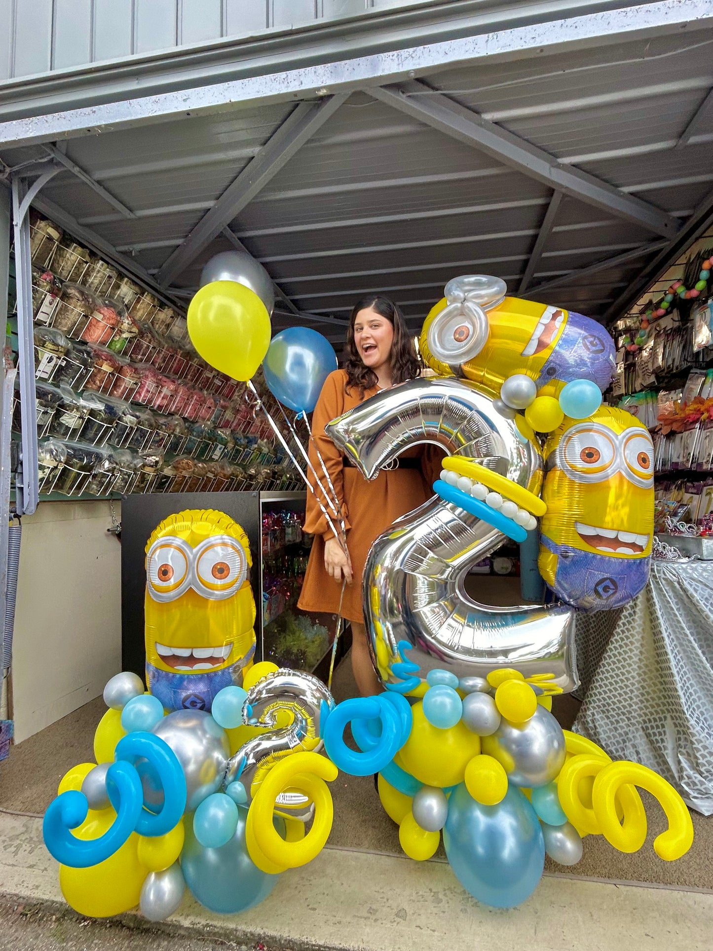 Minion Birthday Balloon Display with Minion character balloons, a large silver number balloon, and festive blue, yellow, and silver balloons.