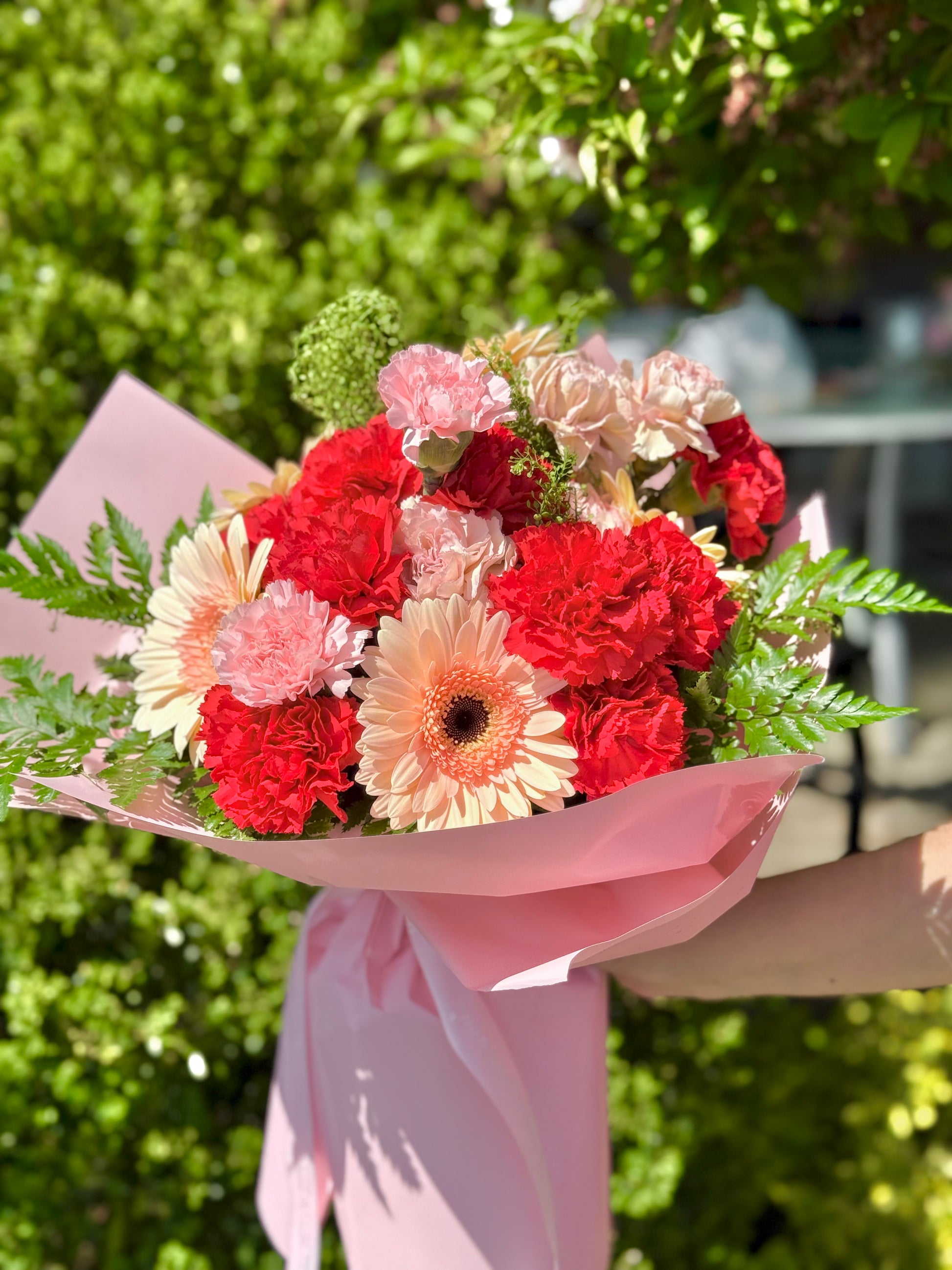 Bouquet of red and pink flowers wrapped in pink paper by wooow flowers.