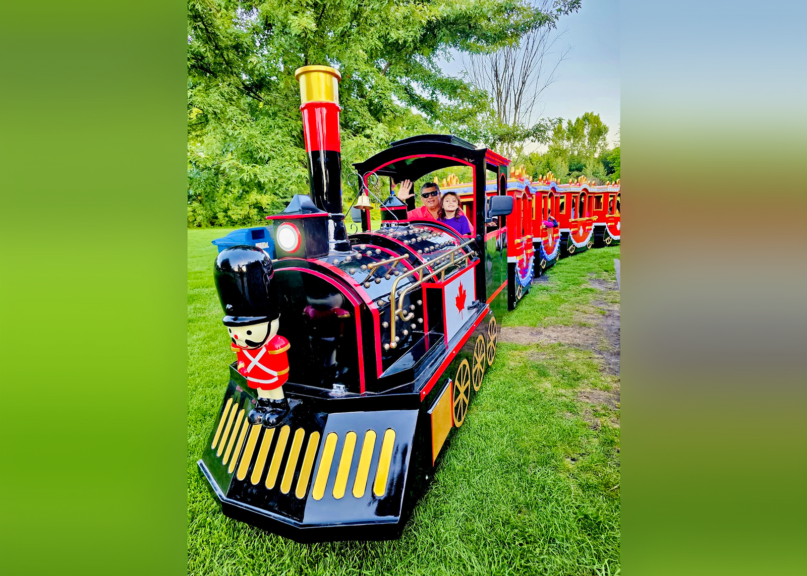 Children's ride-on train on grass with trees in the background