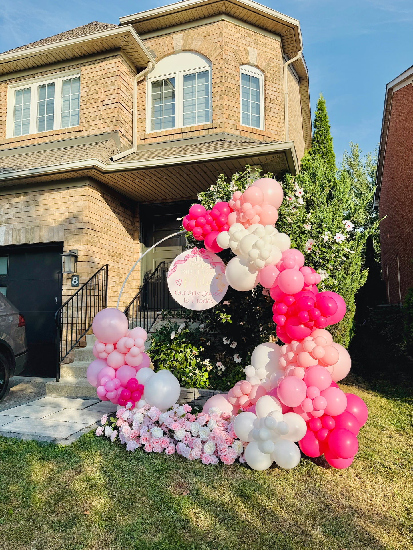 Balloon arch with pink, white, and gray balloons in front of a house.