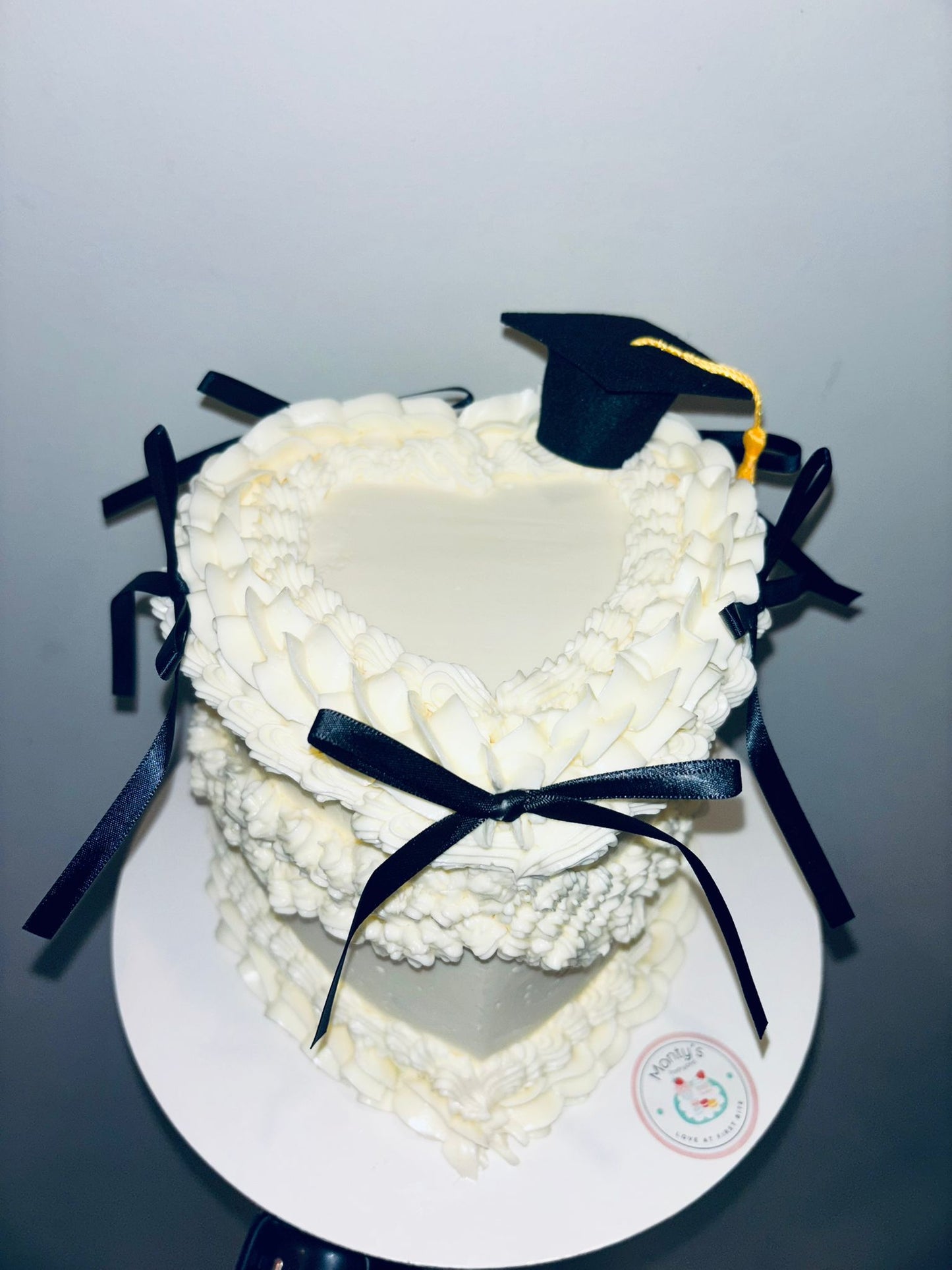 Graduation-themed cake with a white frosting design, black ribbons, and a small graduation cap on a gray background.