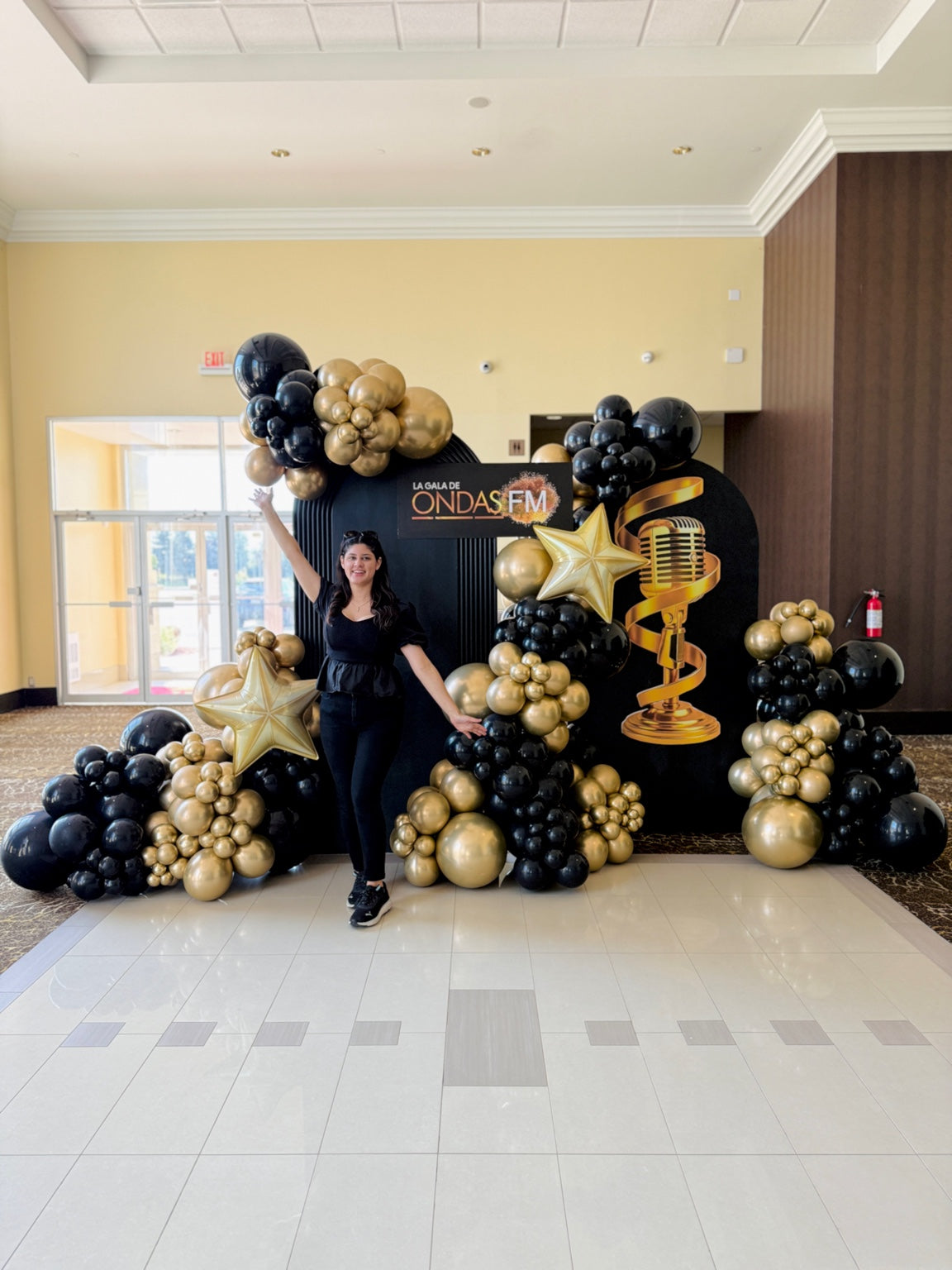 Event decorator standing beside luxury black and gold balloon installation for Ondas FM Gala Toronto.