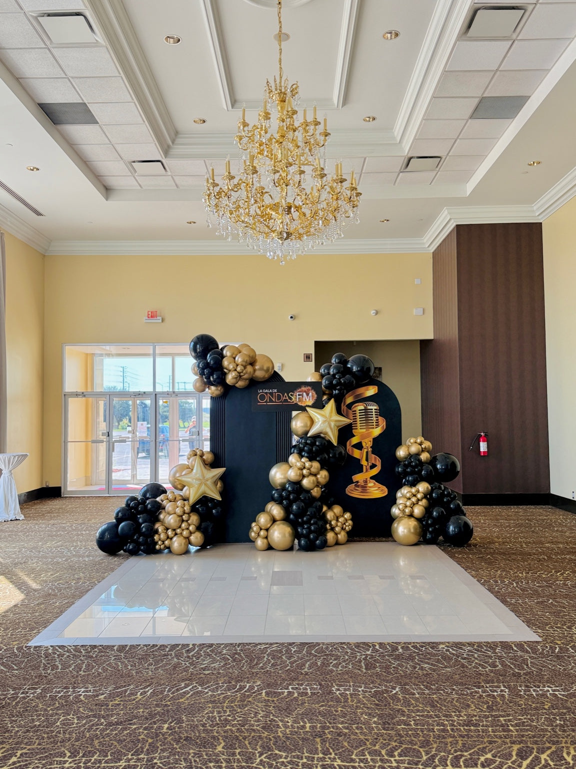 Glamorous black and gold balloon decor with chandelier and custom backdrop for Toronto gala event.
