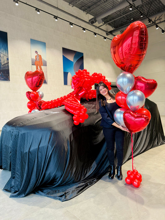 Dealership car reveal setup with giant balloon bow and heart balloon bouquets