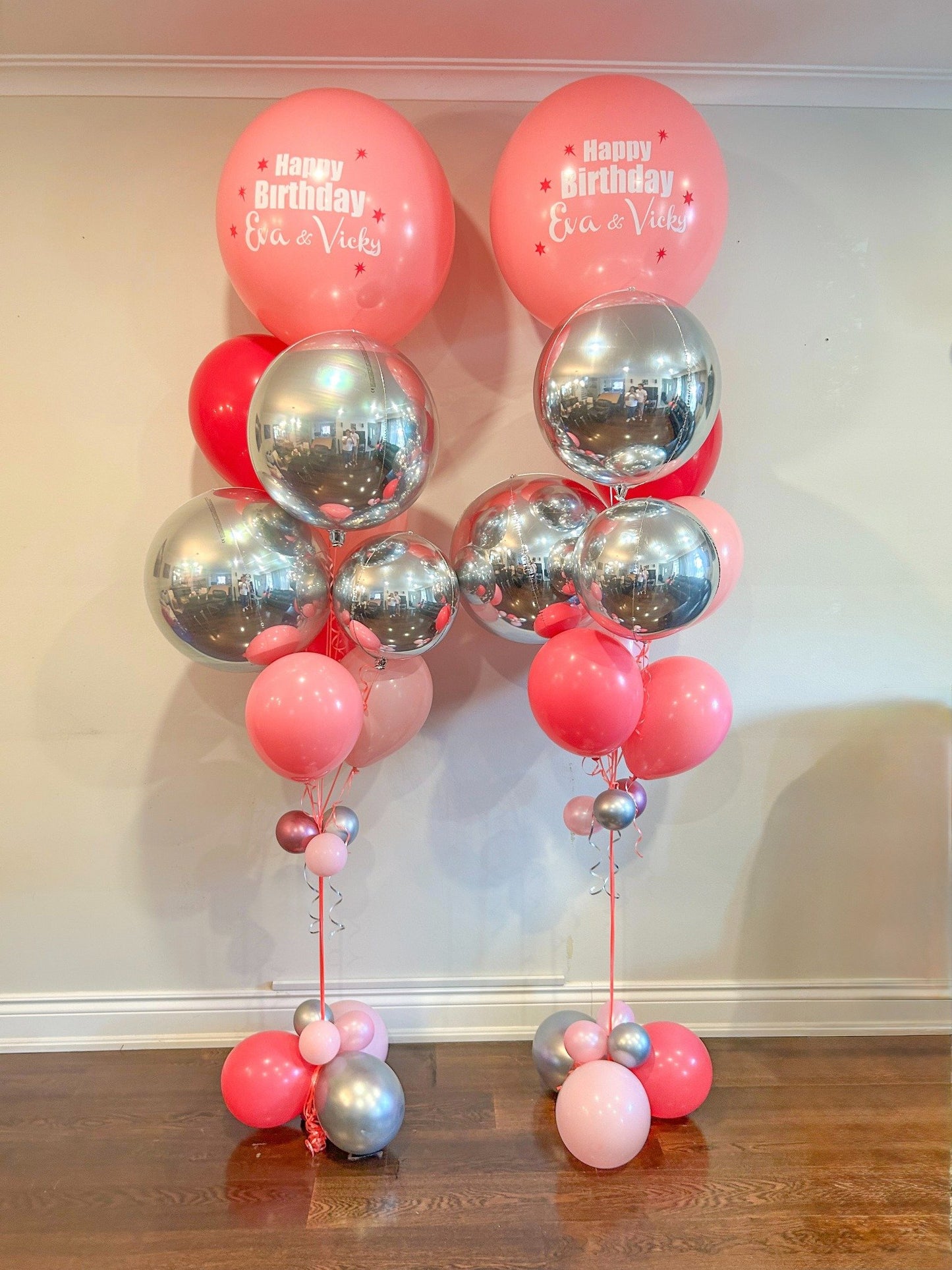 Balloon arrangement with pink and silver balloons on a wooden floor against a white wall.