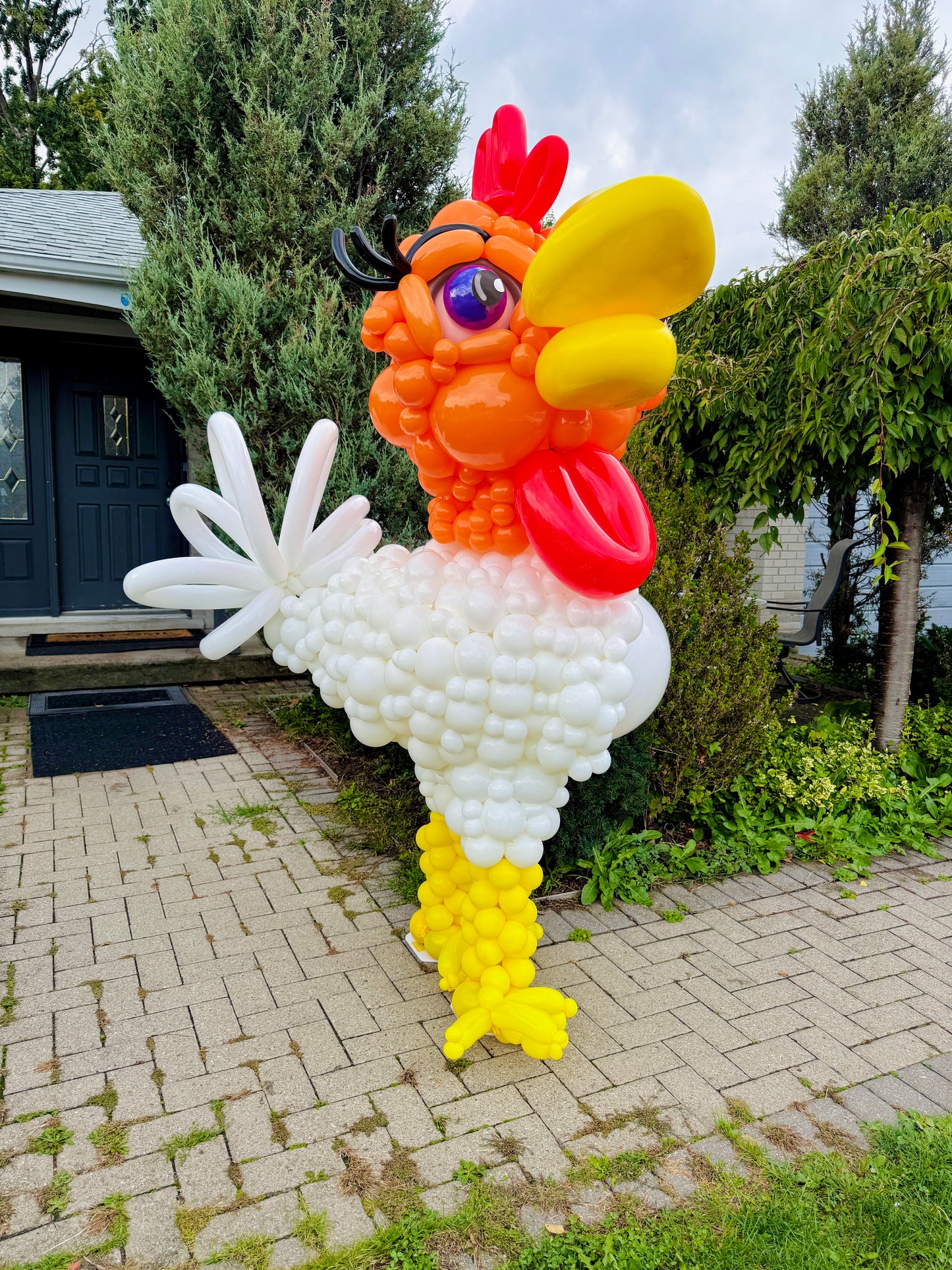 Balloon sculpture of a rooster in front of a house