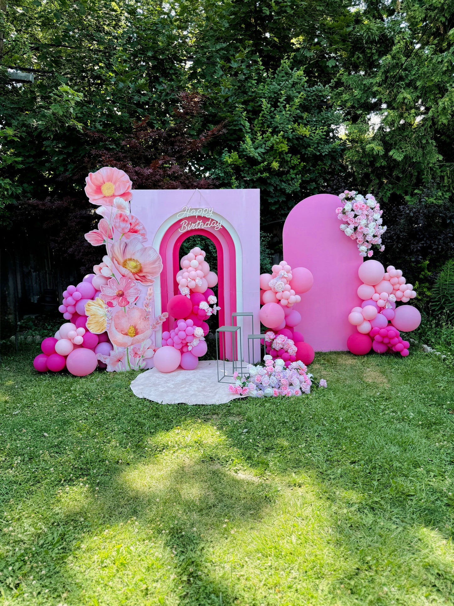 Pink balloon arch and floral decorations on a grassy area with trees in the background