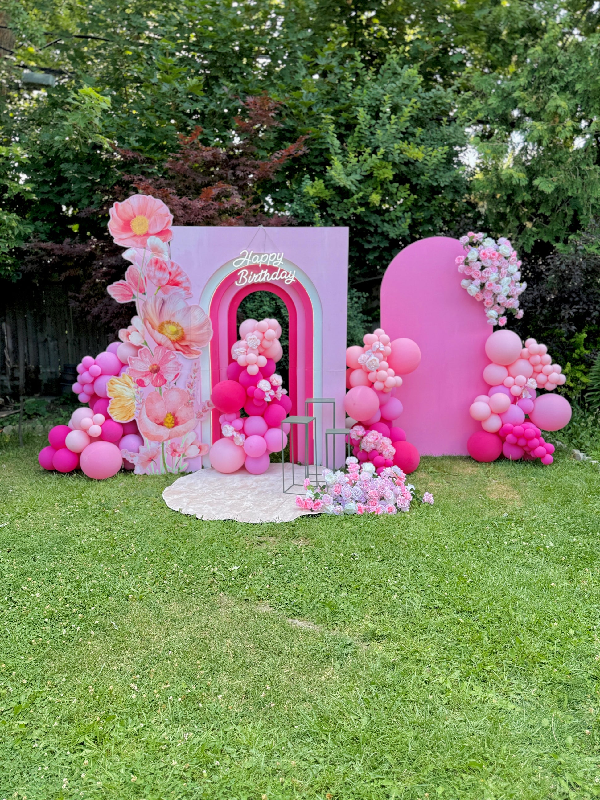 Pink birthday archway with balloons and flowers in a garden setting