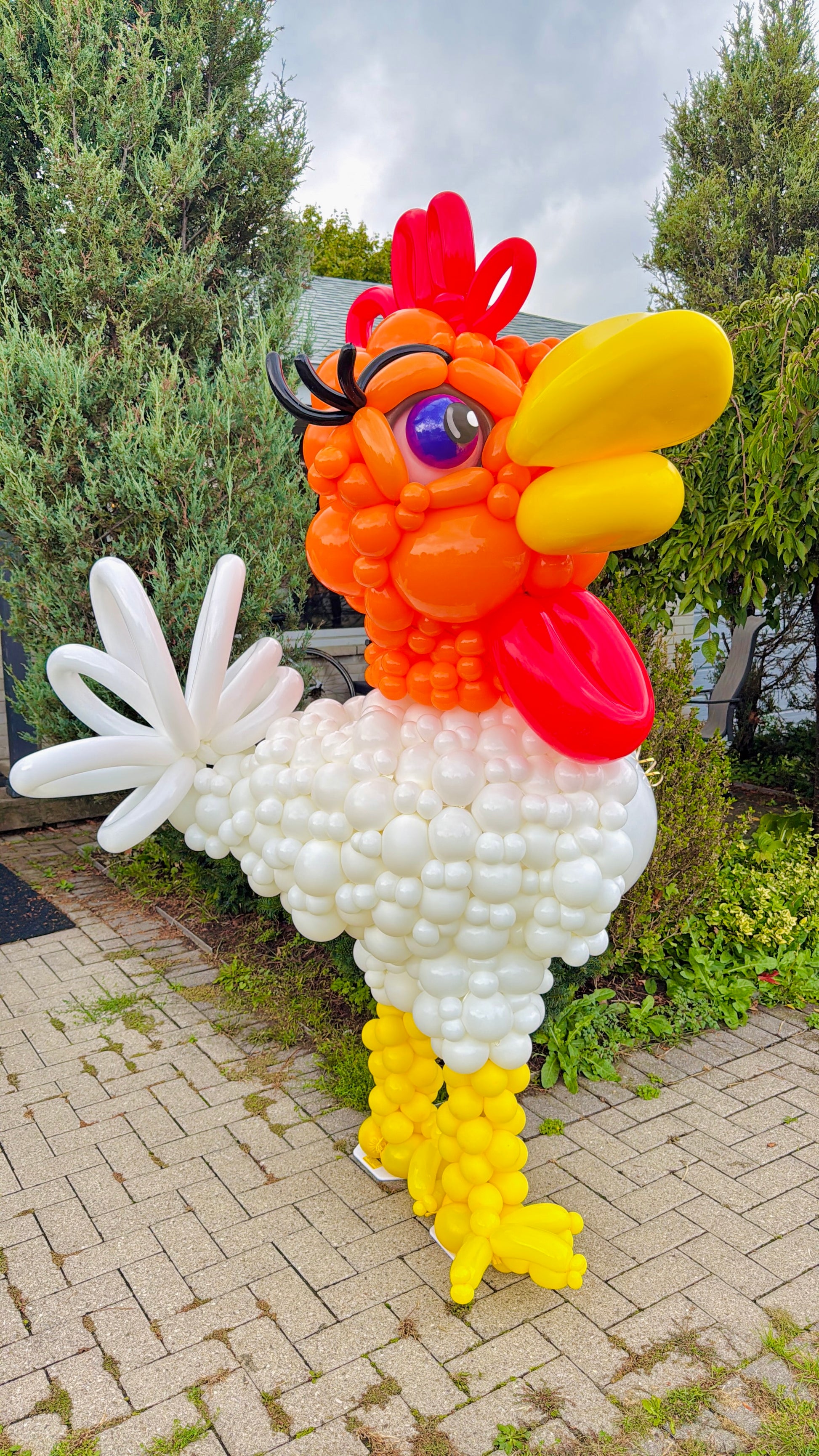 Balloon sculpture of a rooster in an outdoor setting with greenery.