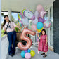 Woman and child with colorful balloons, including a large number '5' balloon, on a balcony.