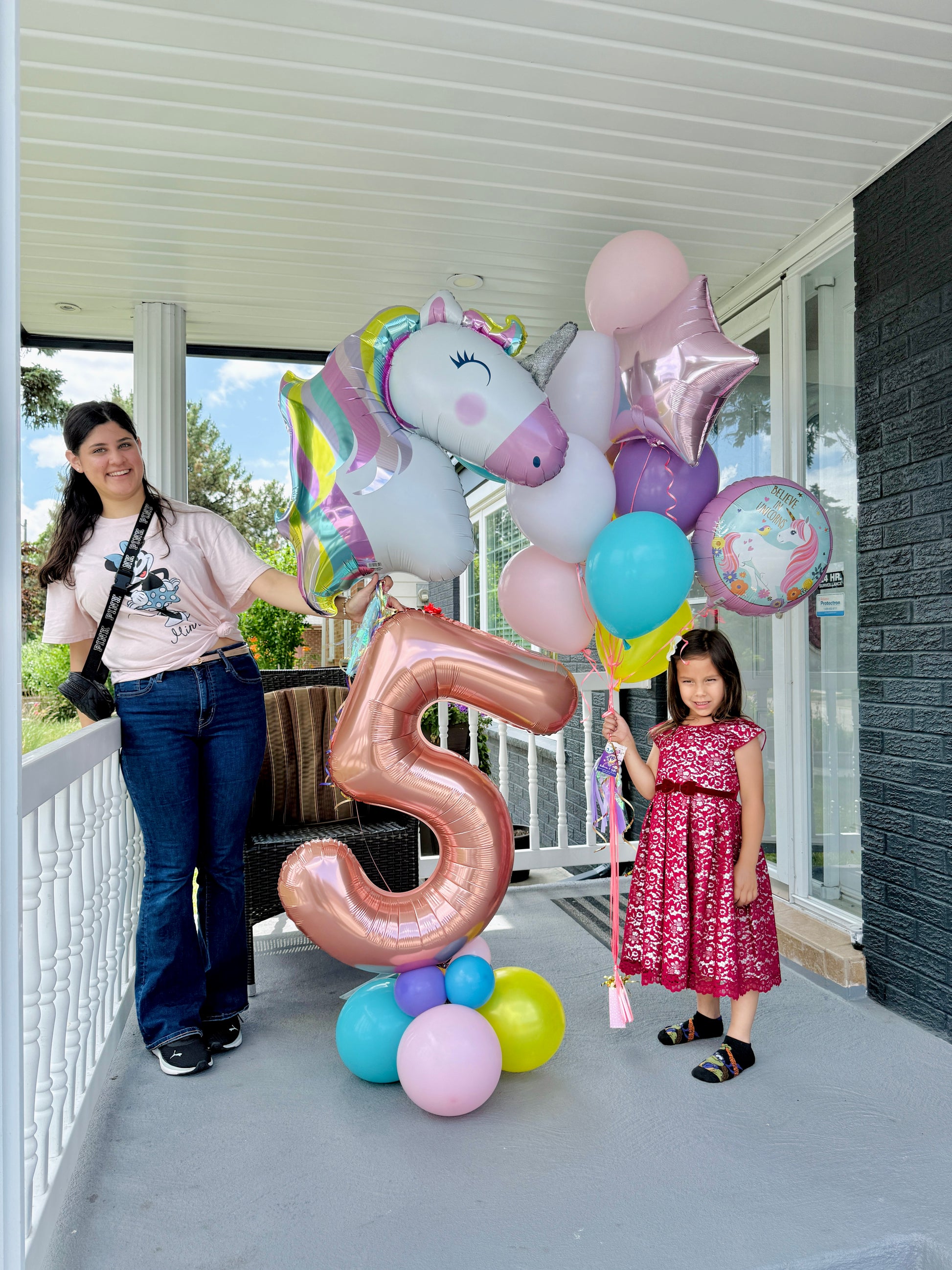 Woman and child with colorful balloons, including a large number '5' balloon, on a balcony.