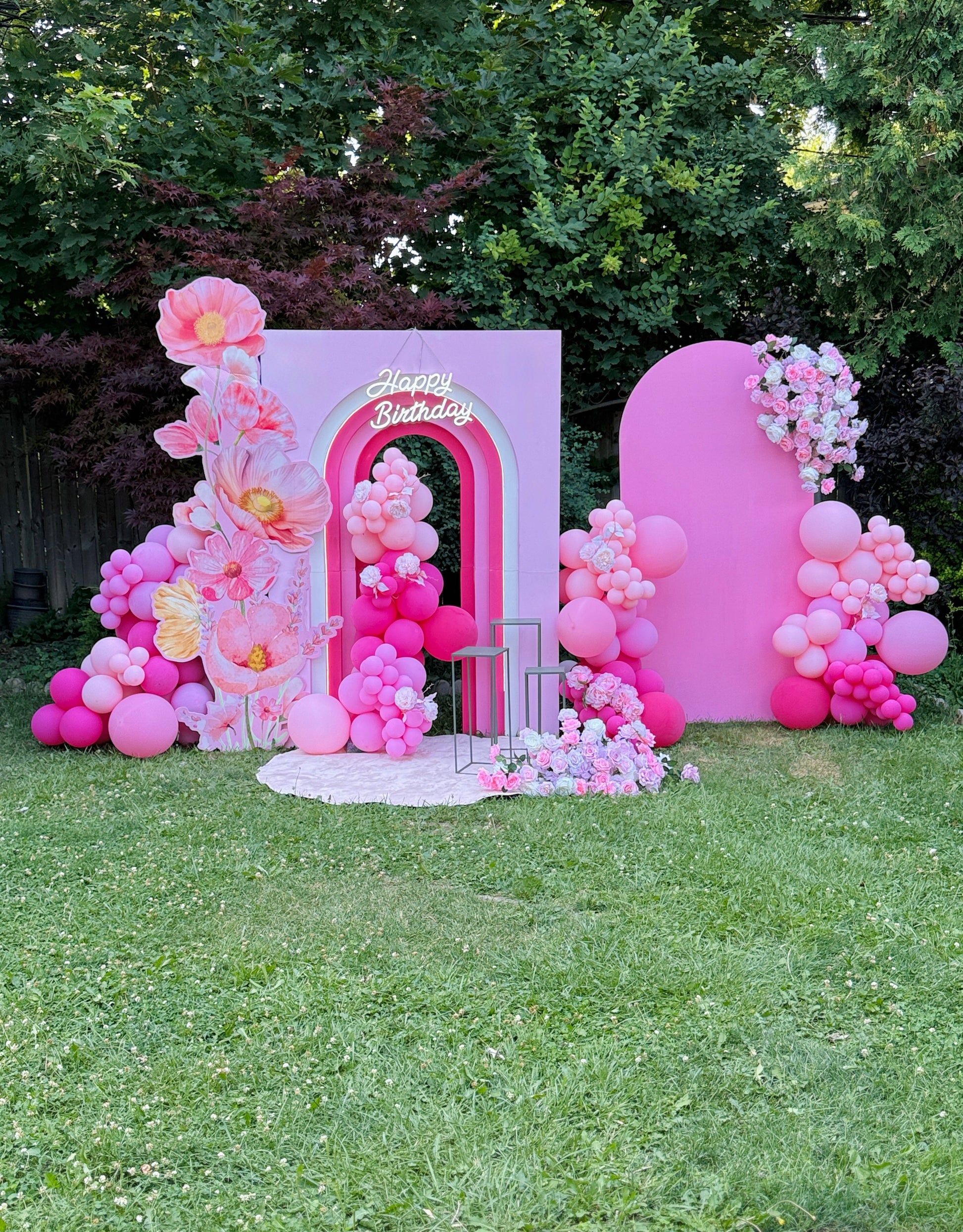 Pink birthday backdrop with balloons and flowers on a grassy area