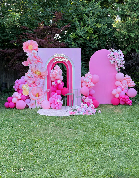 Pink birthday backdrop with balloons and flowers on a grassy area