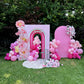 Decorative arch with pink balloons and floral arrangements on a grassy area