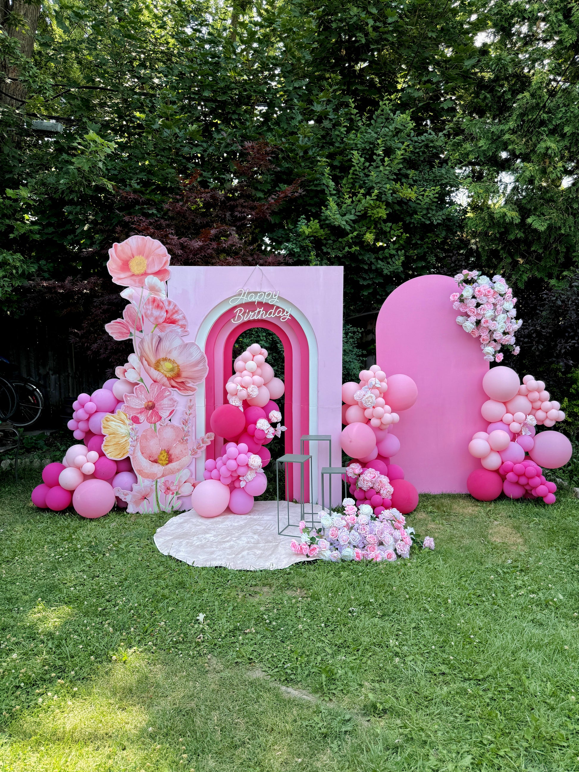 Decorative arch with pink balloons and floral arrangements on a grassy area