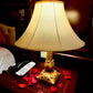 Decorative lamp with a gold base on a wooden table with red flowers and a phone.