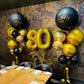 Decorative balloons with 'Happy Birthday DADI' and number '80' in a dining setting.