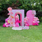 Pink birthday arch with balloons and flowers on a grassy outdoor setting