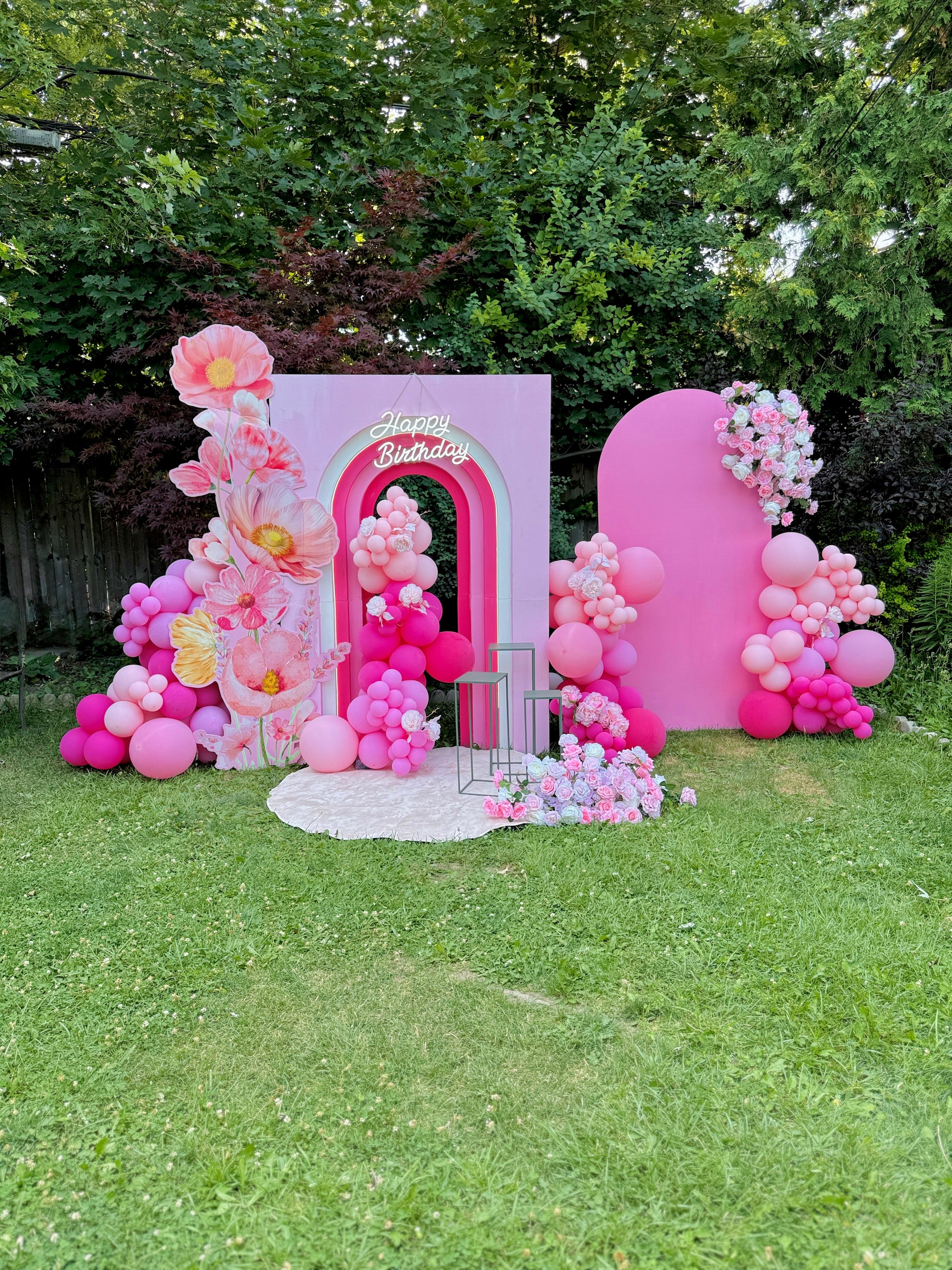 Pink birthday arch with balloons and flowers on a grassy outdoor setting