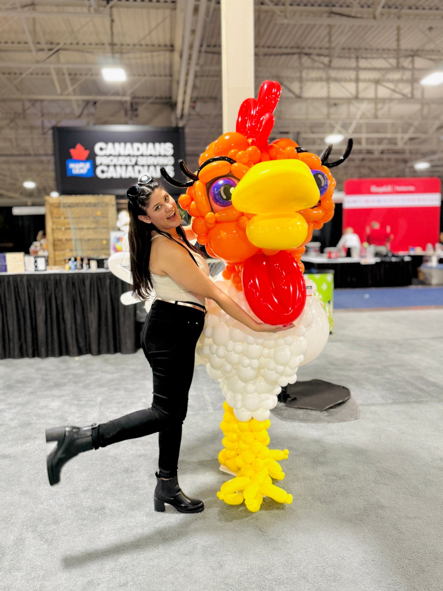 Person posing with a large balloon rooster at an event.
