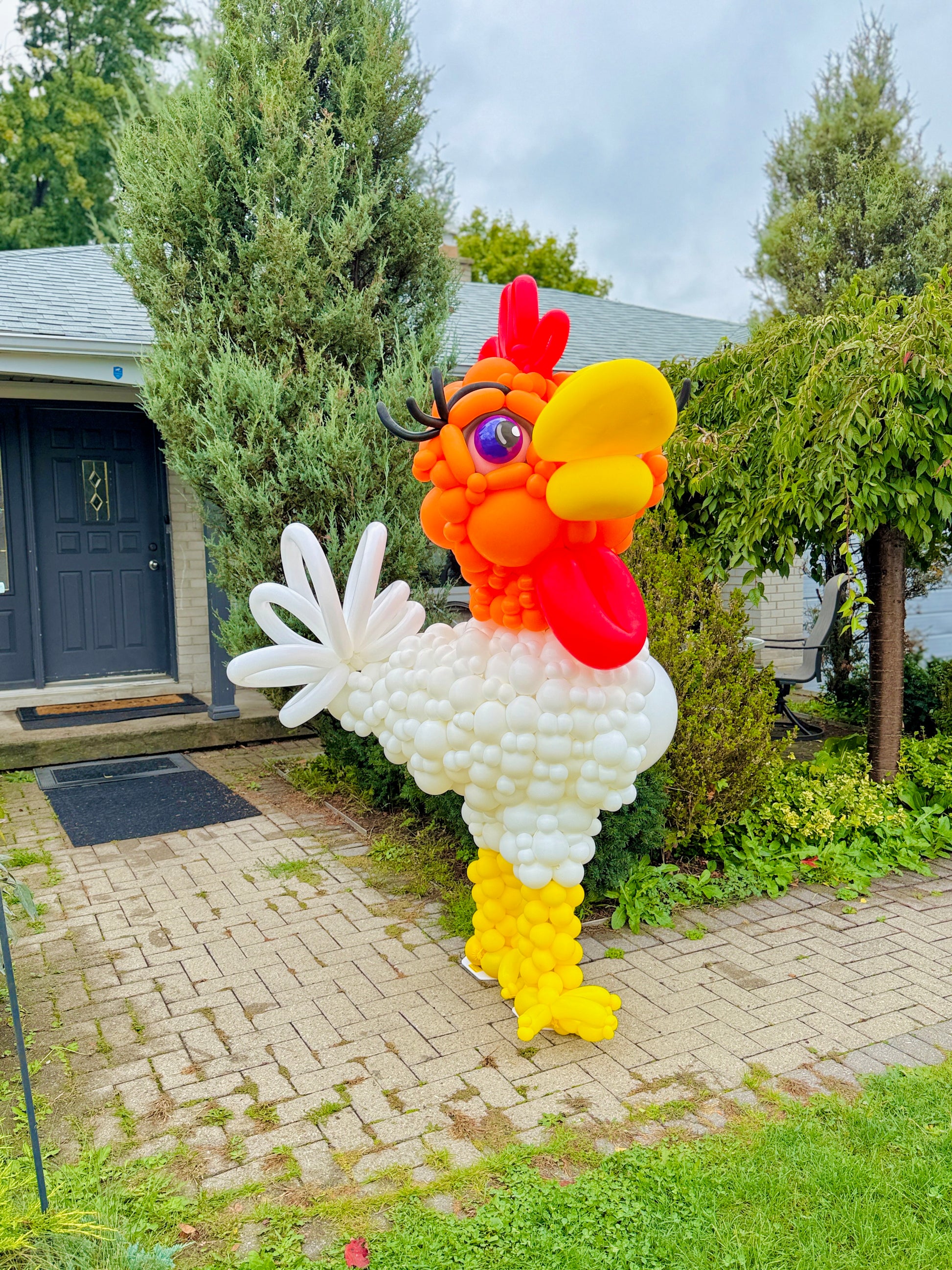 Balloon sculpture of a rooster in front of a house