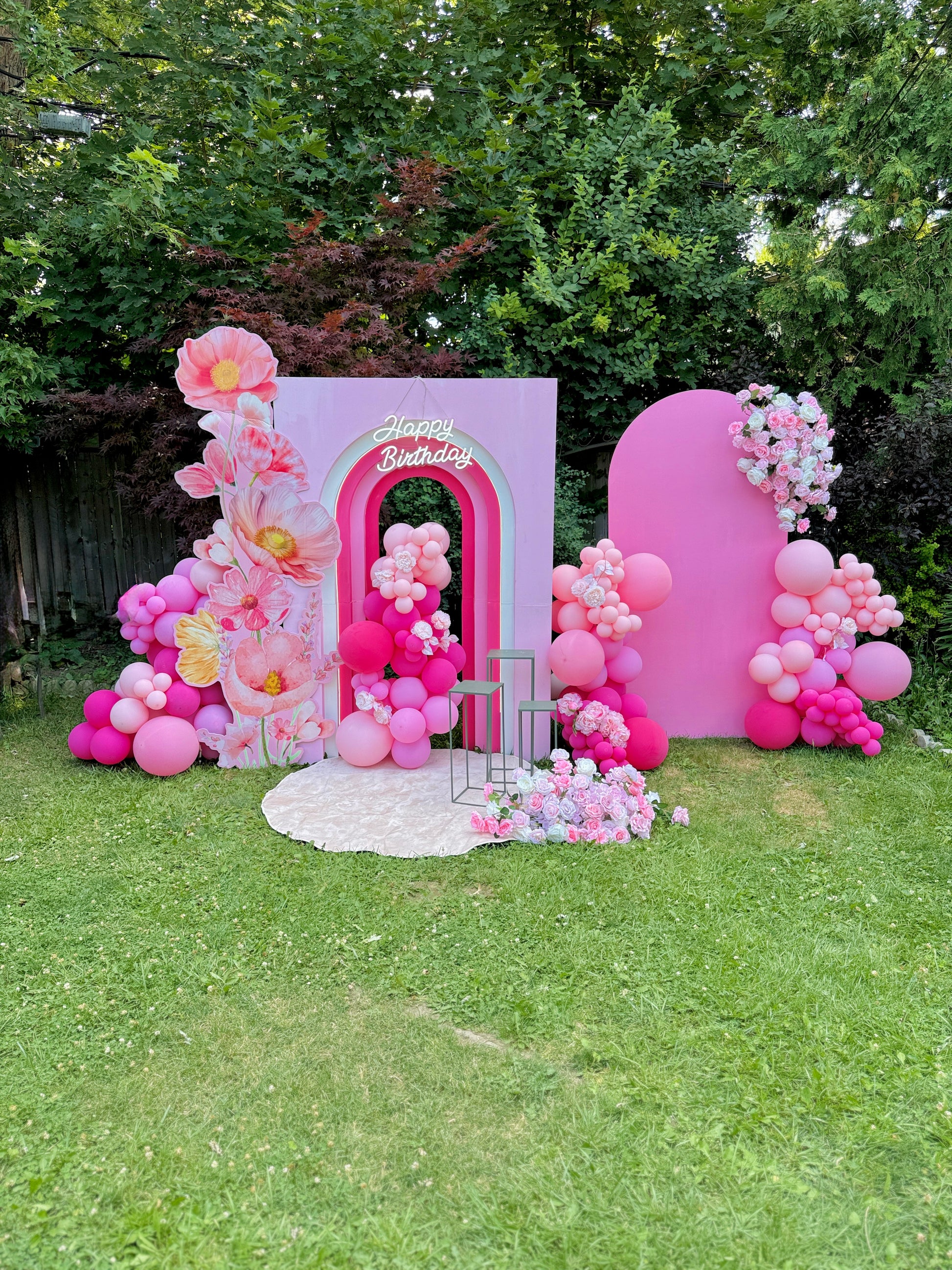 Pink birthday arch with balloons and flowers in a garden setting