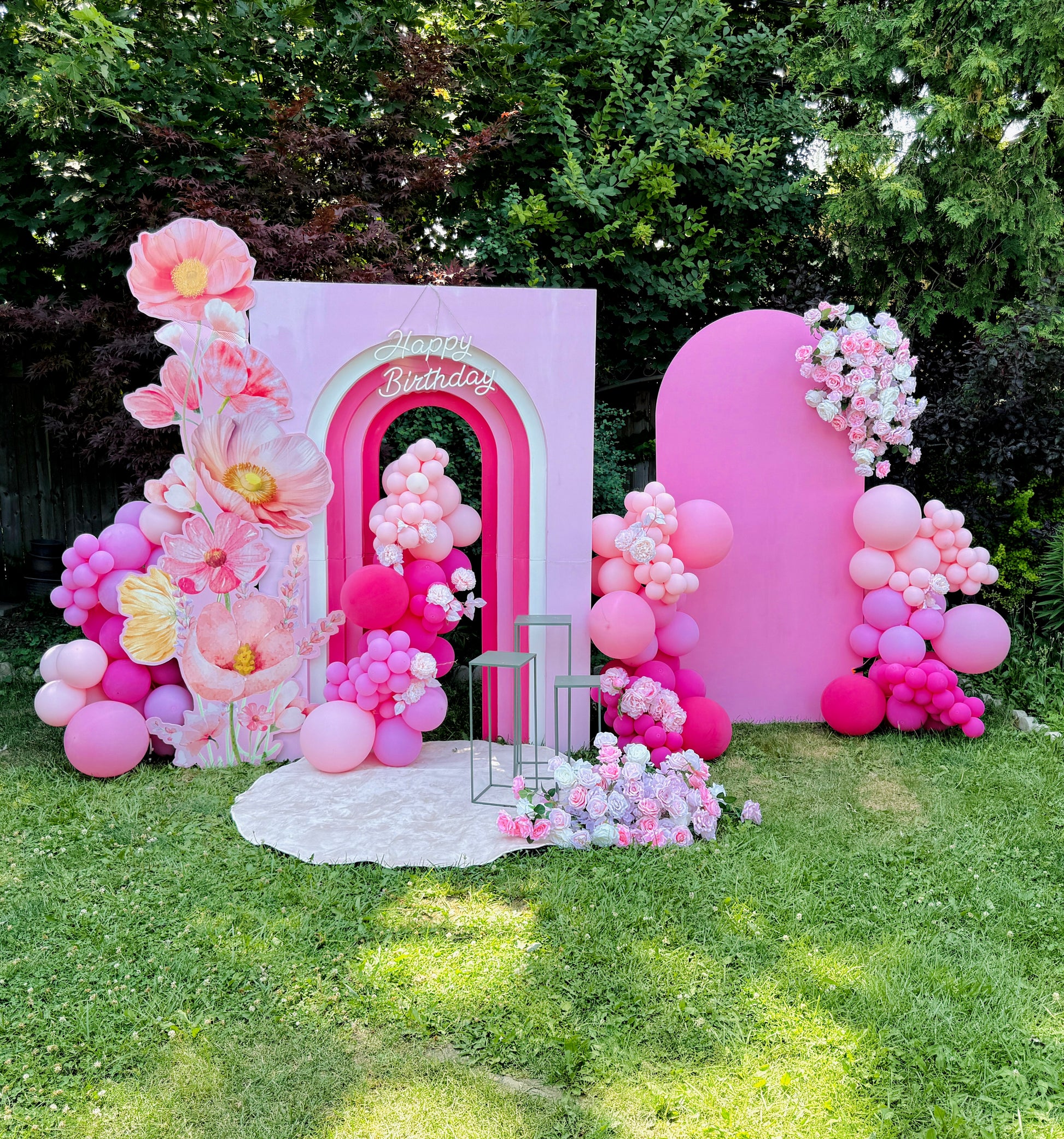 Pink birthday arch with balloons and flowers in a garden setting