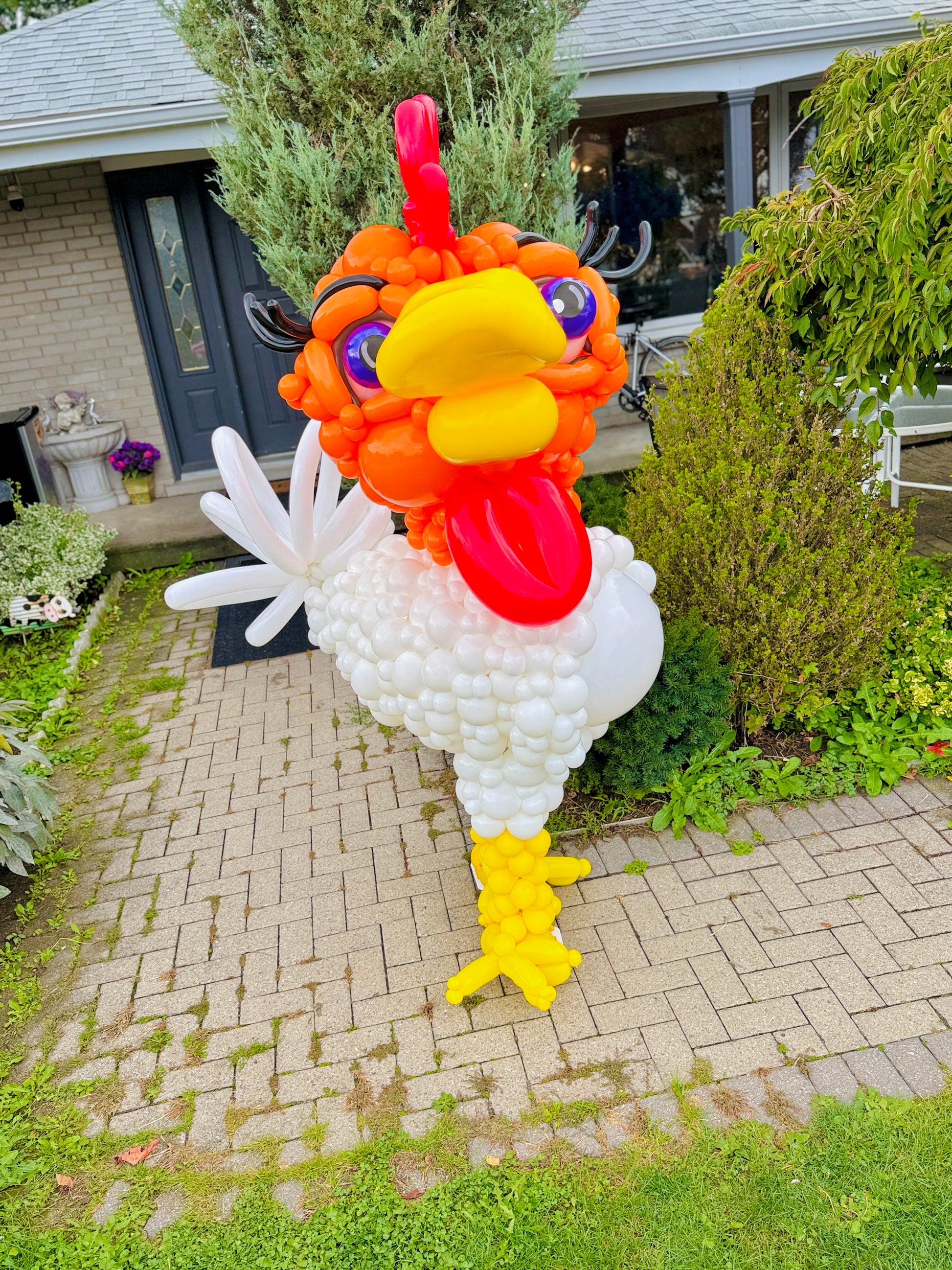 Balloon sculpture of a rooster in front of a house