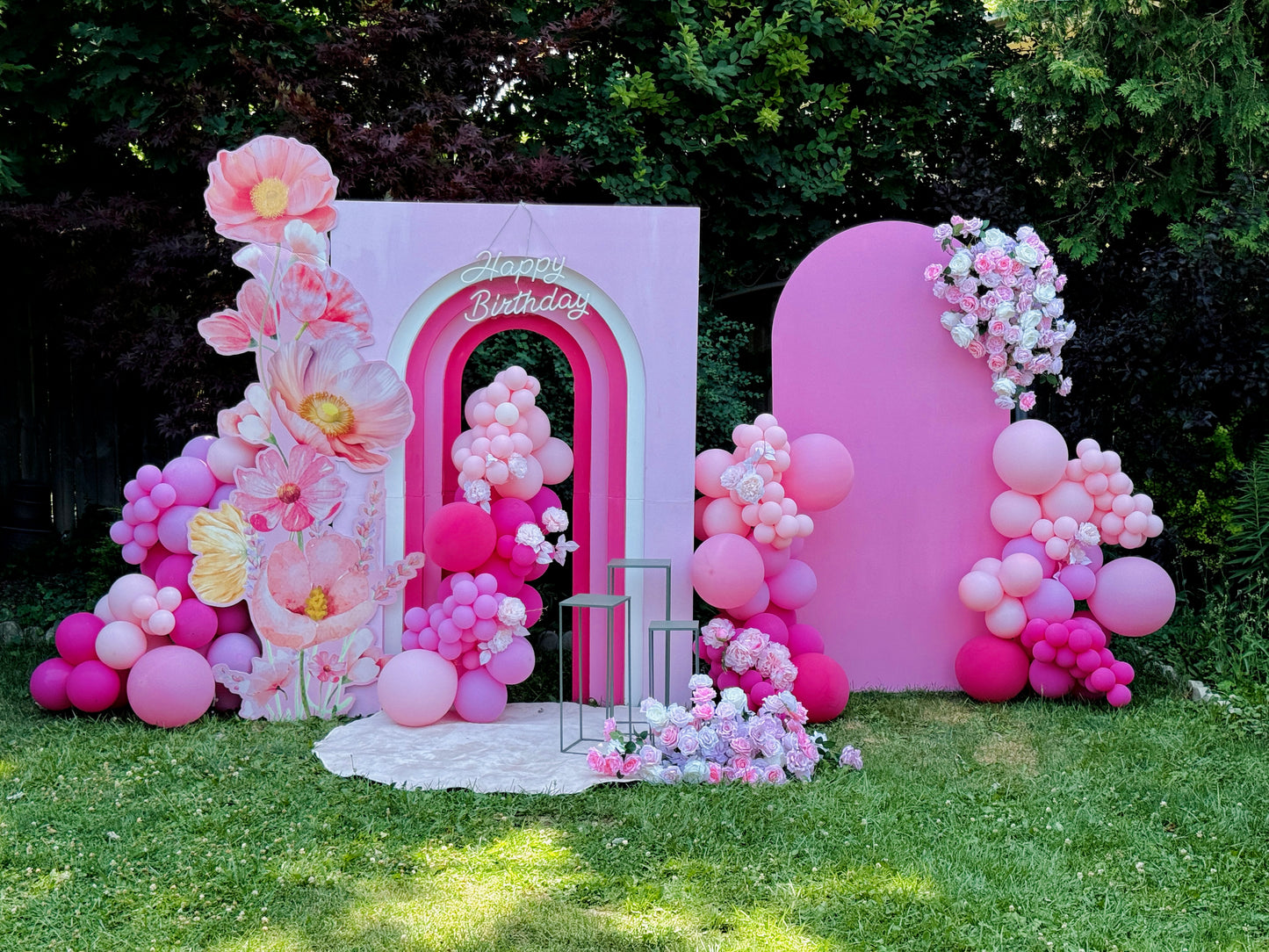 Decorative arch with pink balloons and flowers on a grassy area