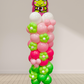 Balloon column with pink and green flowers and a cartoon frog character on top against a white wall.