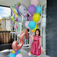 Child holding balloons with a large number 5 balloon on a porch.