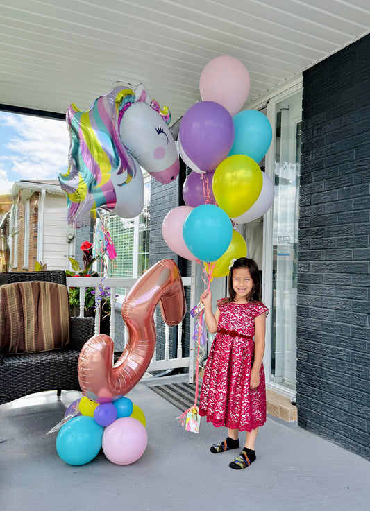Child holding balloons with a large number 5 balloon on a porch.